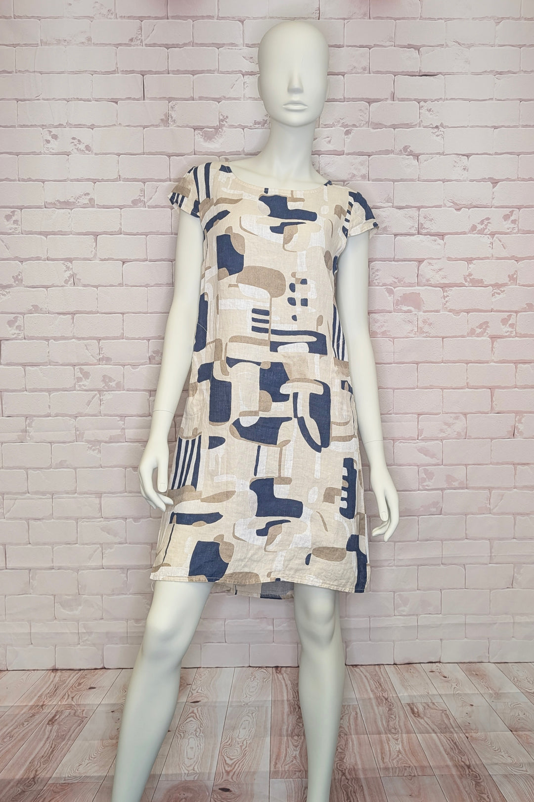 Mannequin wearing a patterned linen dress against a white brick wall.