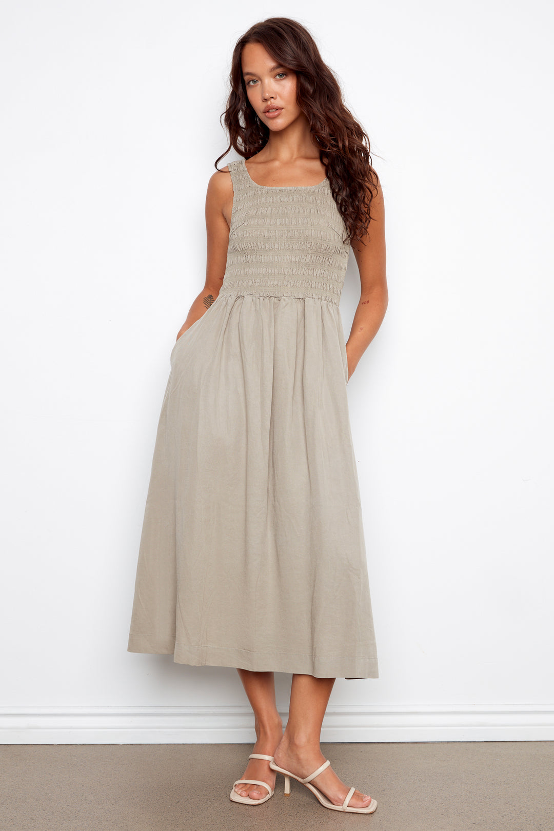 Woman wearing a beige sleeveless dress against a white background