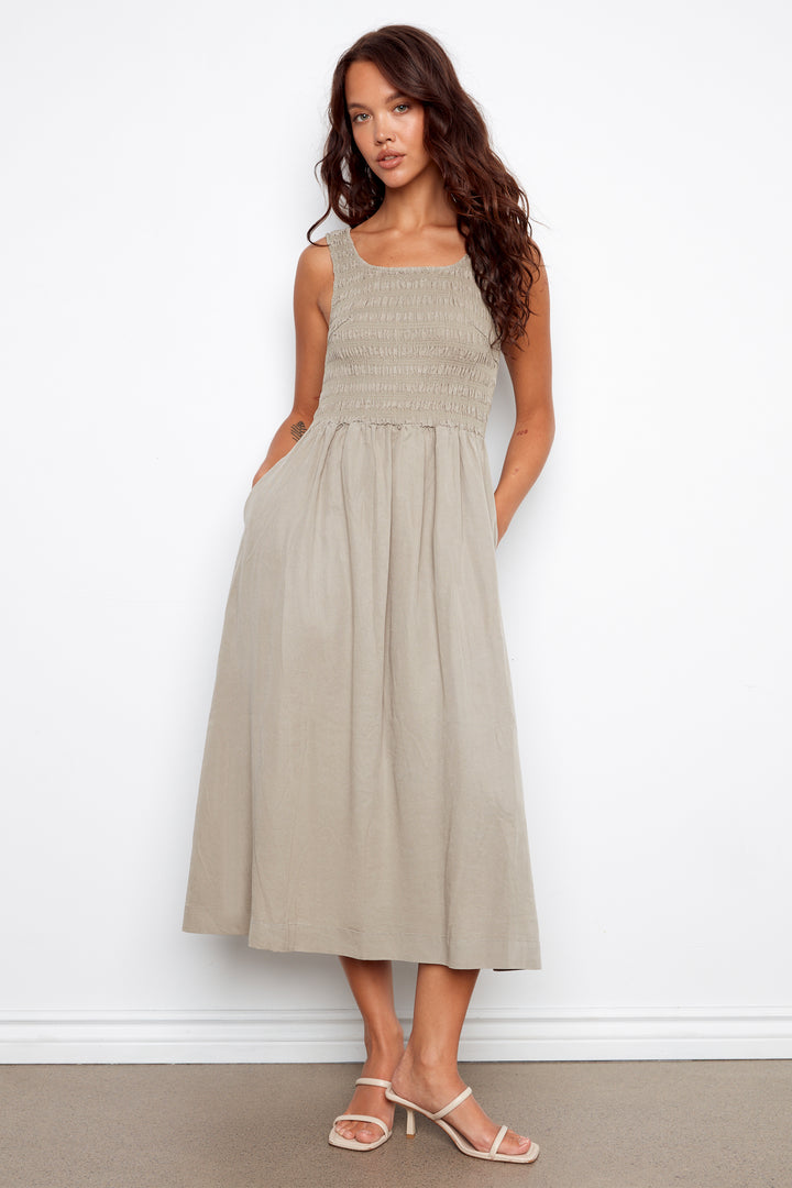 Woman wearing a beige sleeveless dress against a white background