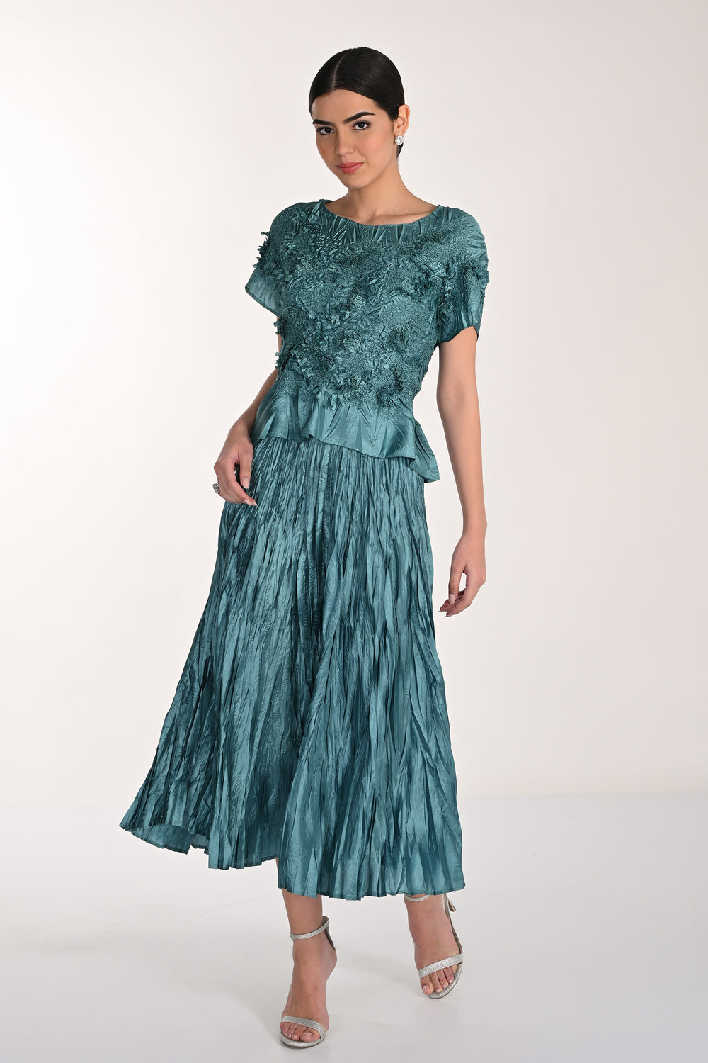 Woman wearing a teal skirt and top with a textured top and pleated skirt on a white background