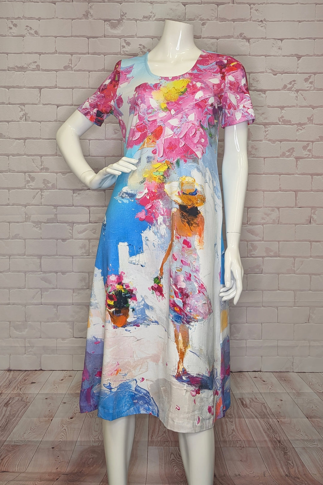 Mannequin wearing a colorful dress with artistic design against a brick wall.