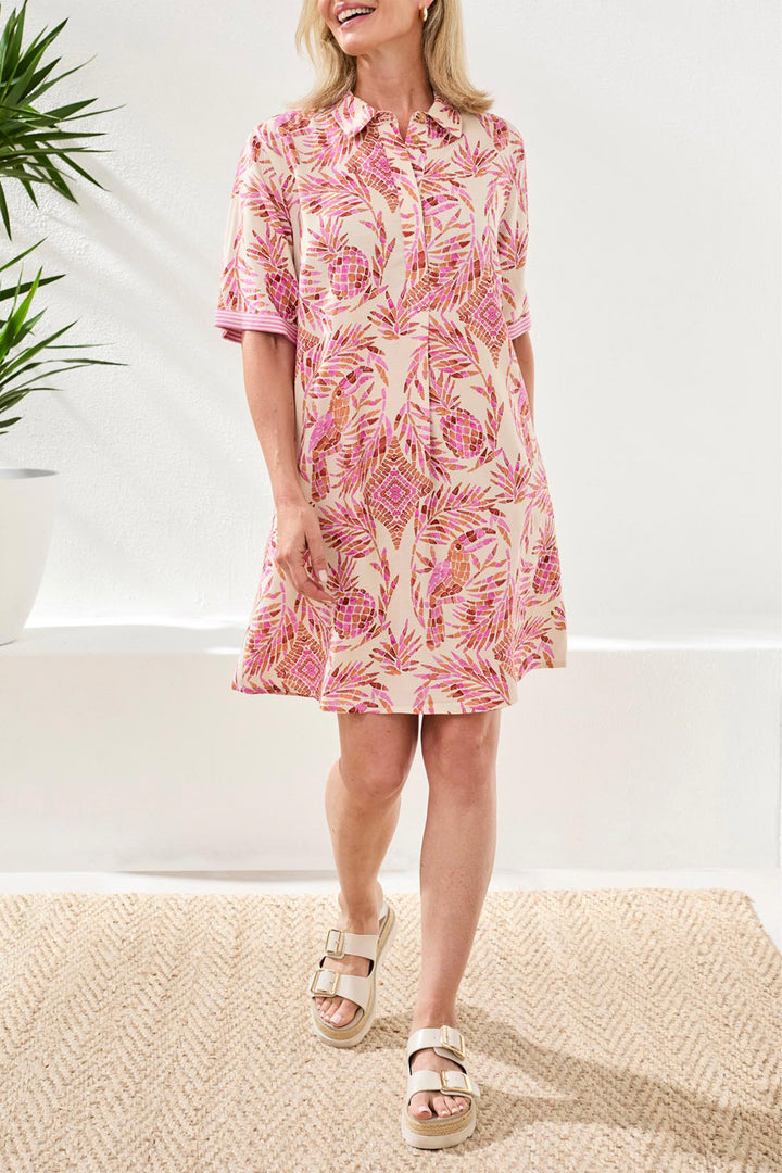 Woman wearing a pink floral summer shift dress standing indoors with a white background