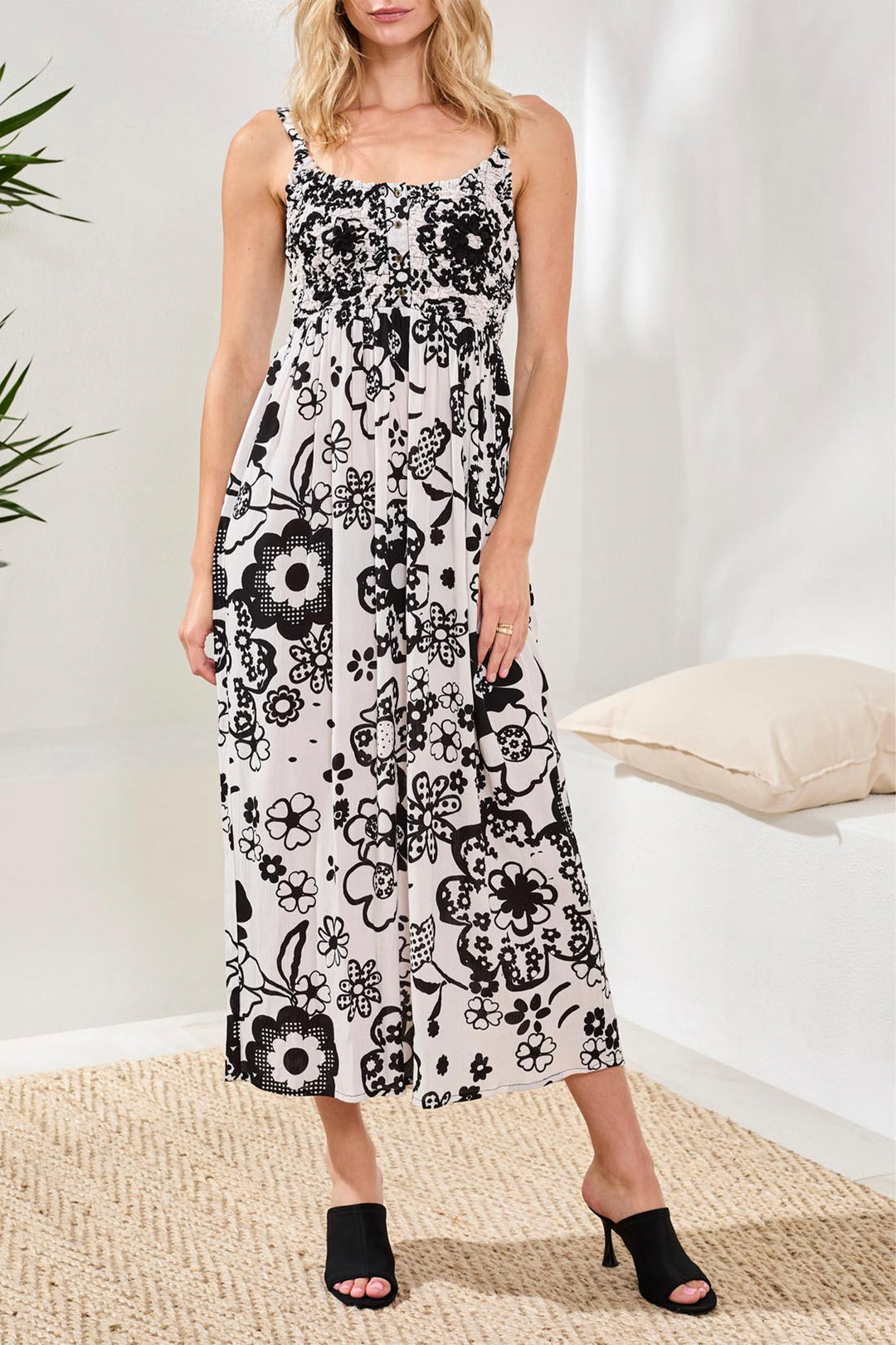 Woman wearing a black and white floral sleeveless dress in a minimal indoor setting.