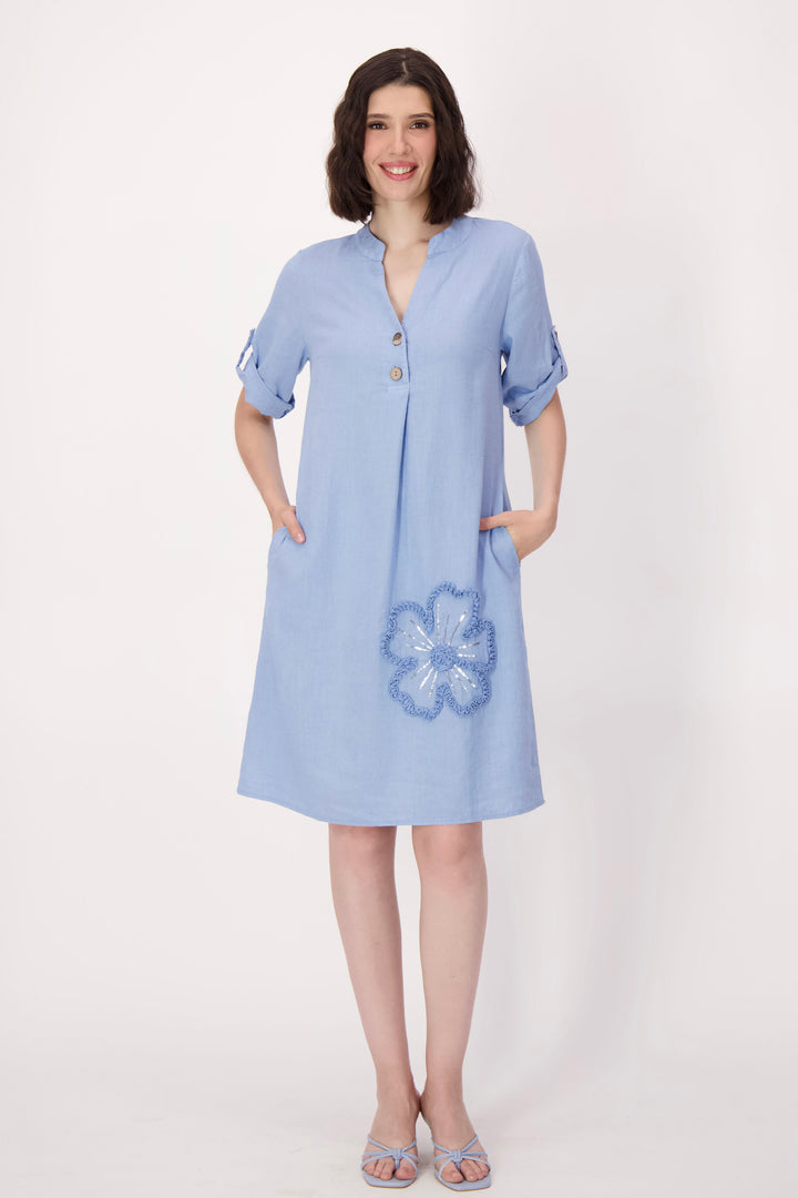 Woman wearing a light blue dress with floral embroidery on a white background