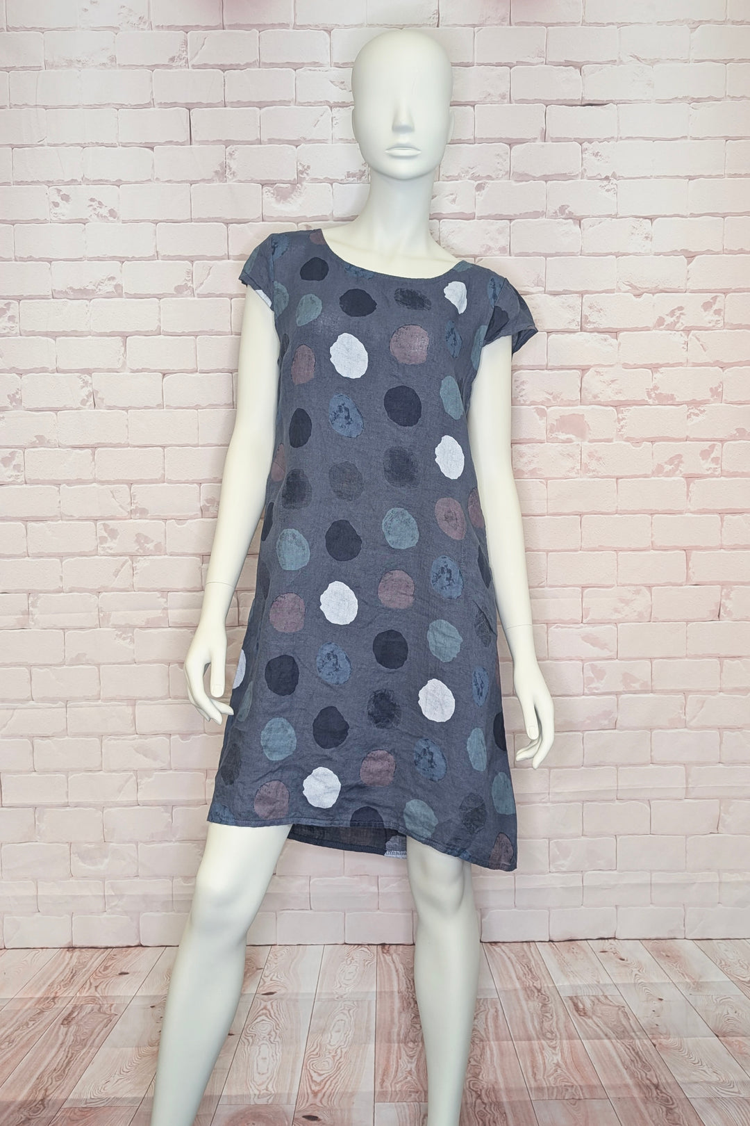 Mannequin wearing a polka dot linen dress against a brick wall.