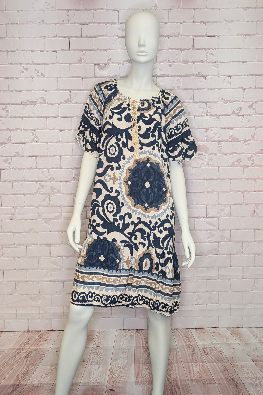 Mannequin wearing a patterned light summer dress against a white brick wall.