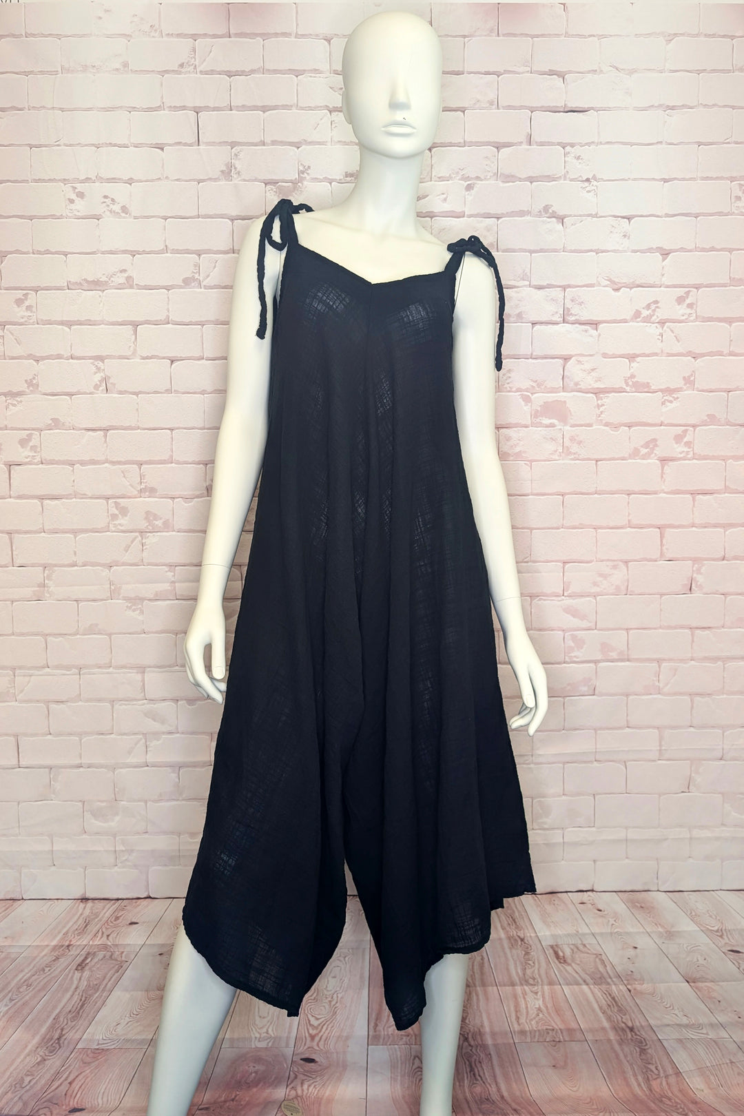 Black romper dress with long tie straps on a mannequin against a light brick wall.
