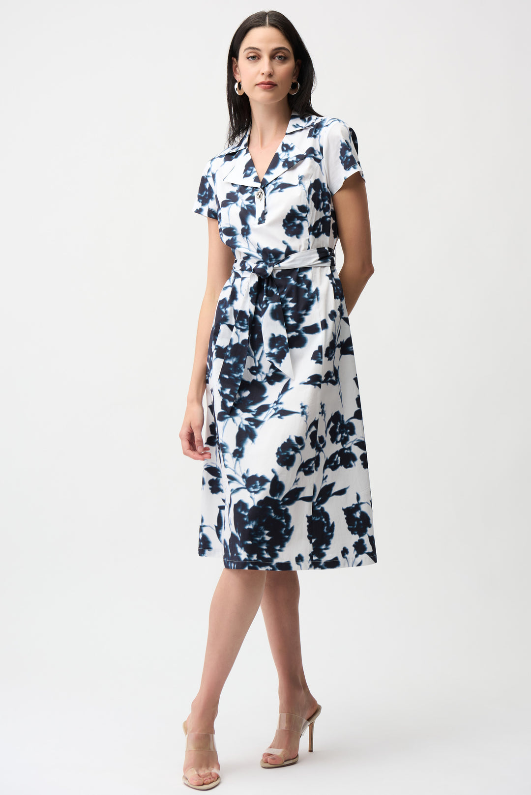 Woman wearing a white dress with blue floral pattern and sash belt on a white background