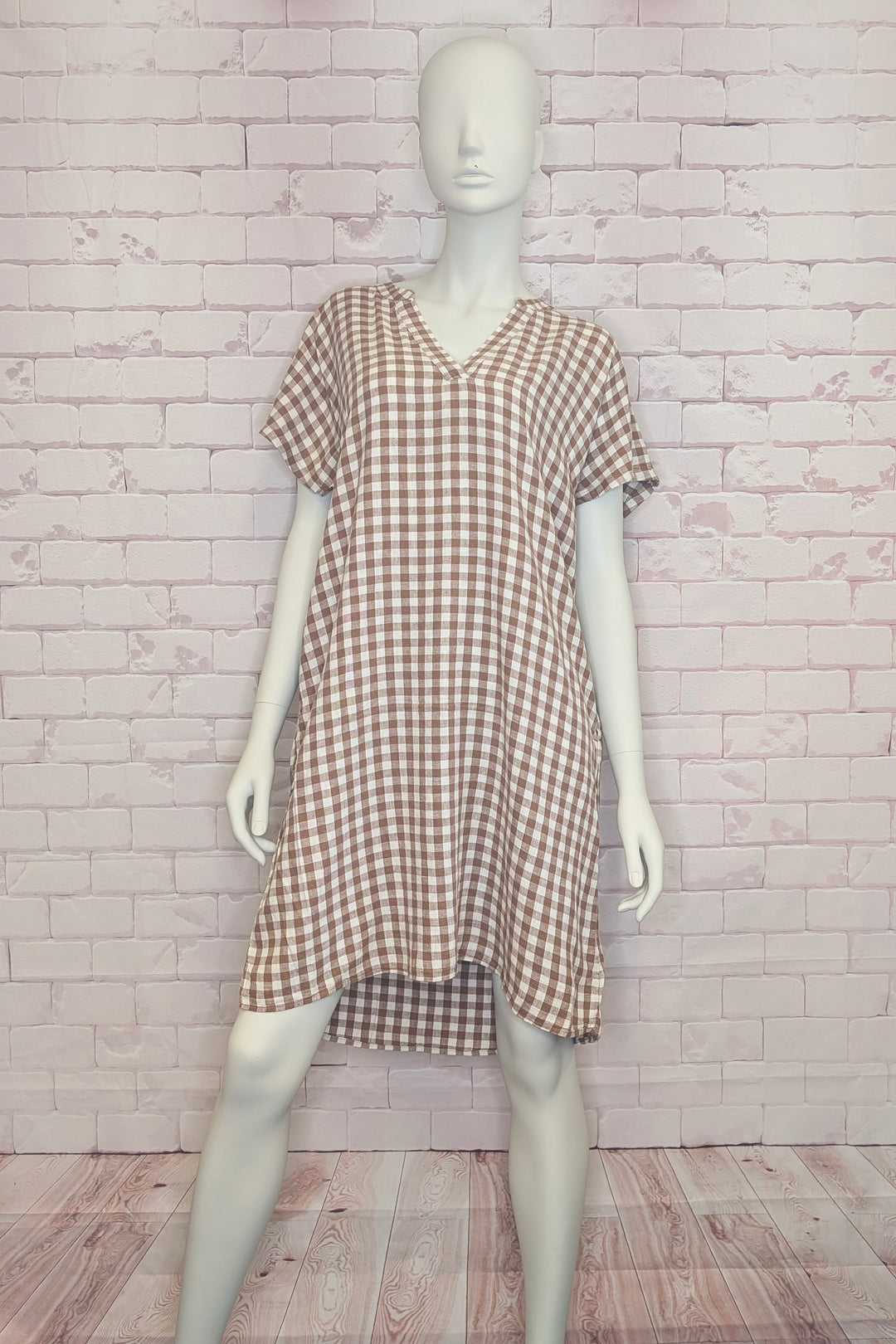 Mannequin wearing a checkered short sleeve dress against a white brick wall.