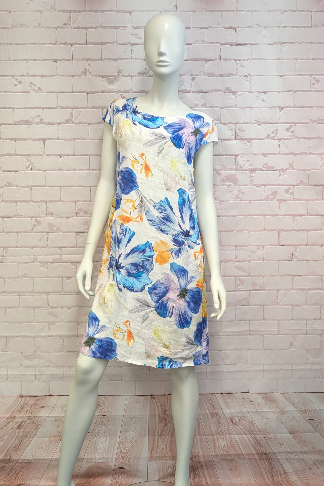 Mannequin wearing a floral short sleeve dress against a white brick wall.
