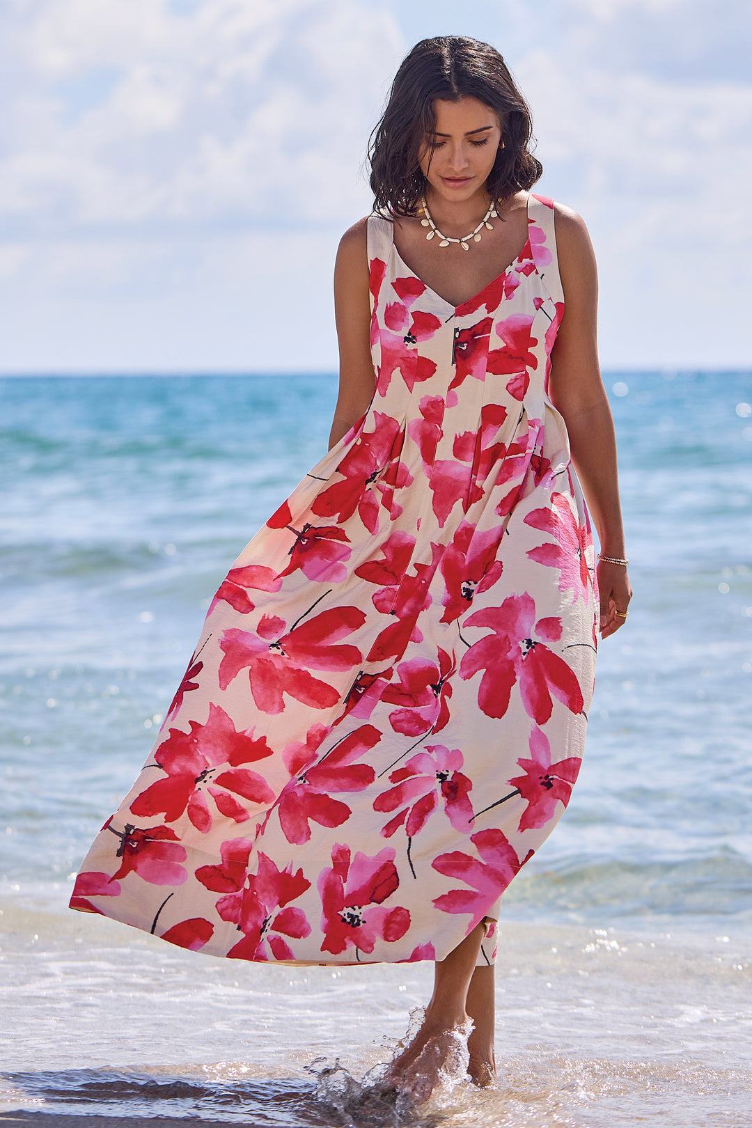 Woman in a floral sleeveless summer dress standing on a beach with ocean in the background