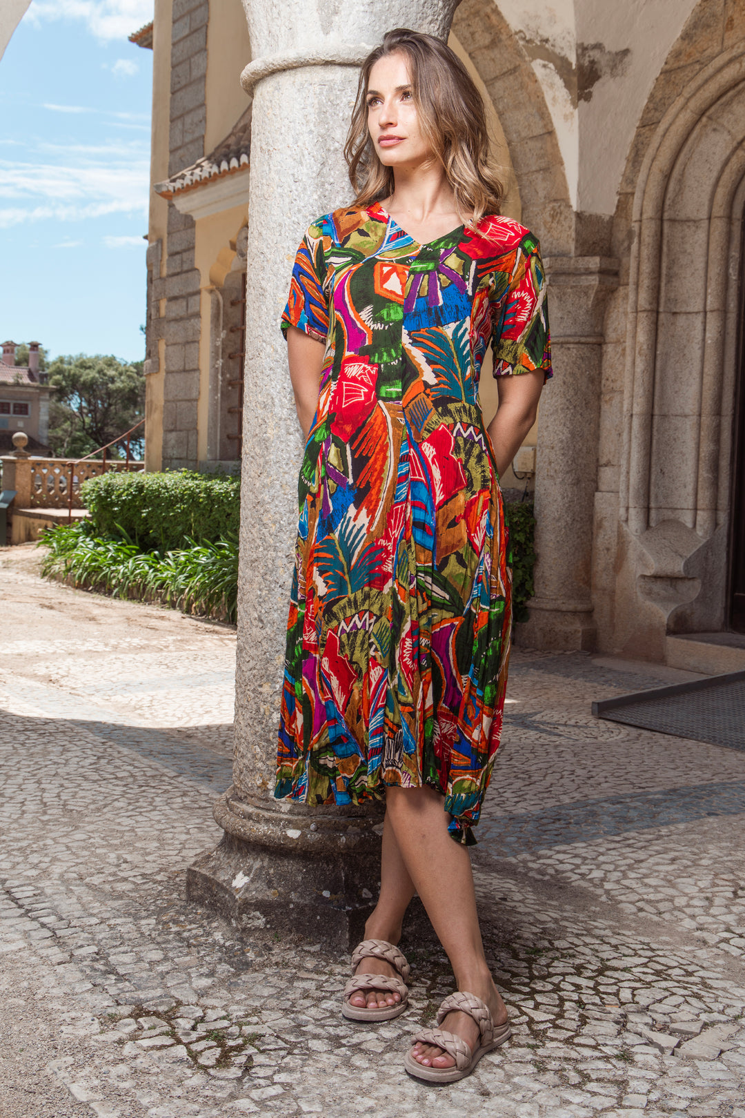 Woman in a colorful v-neck short sleeve dress standing in front of an architectural structure.