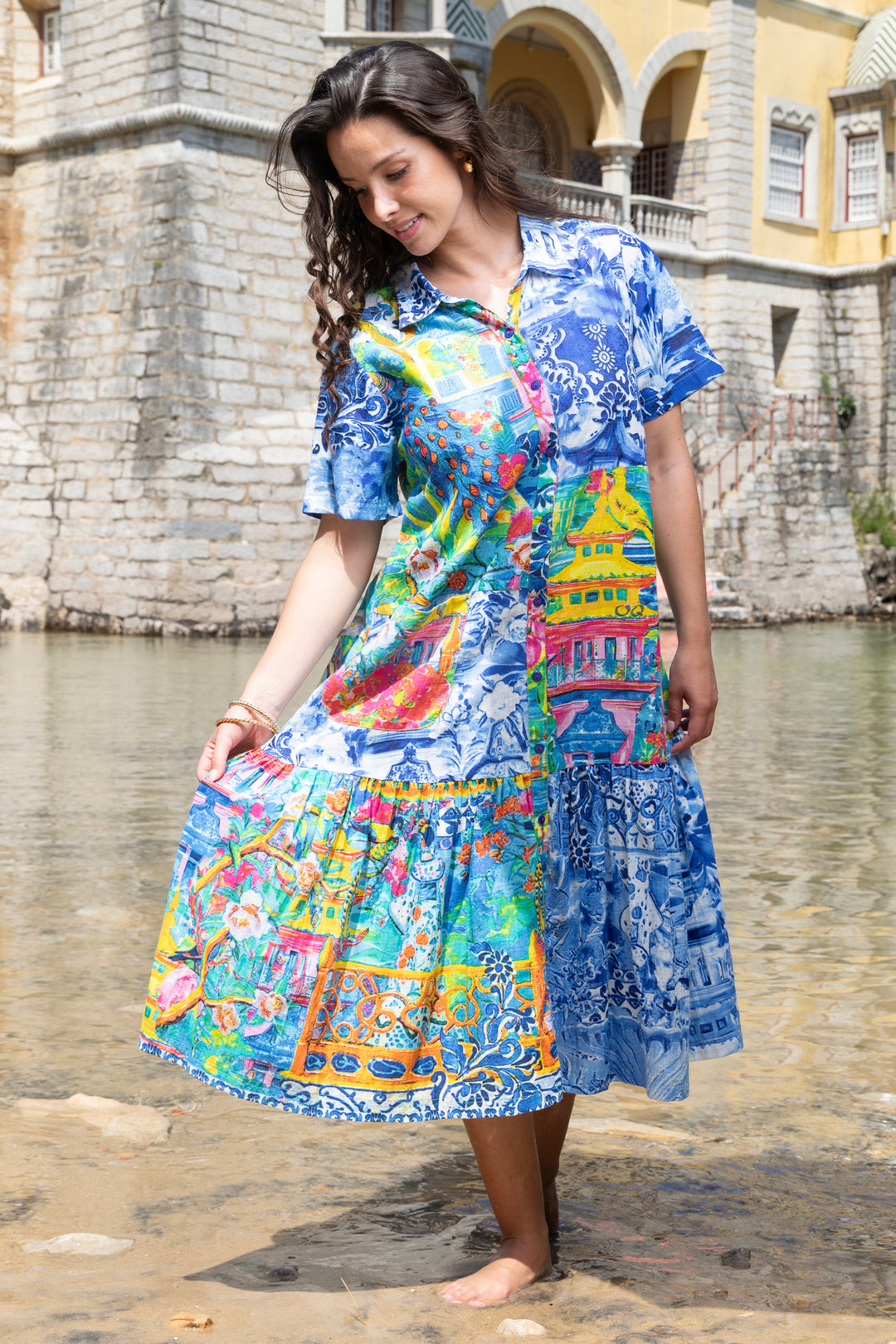 Woman wearing a colorful cotton shirt dress standing by a body of water with a building in the background