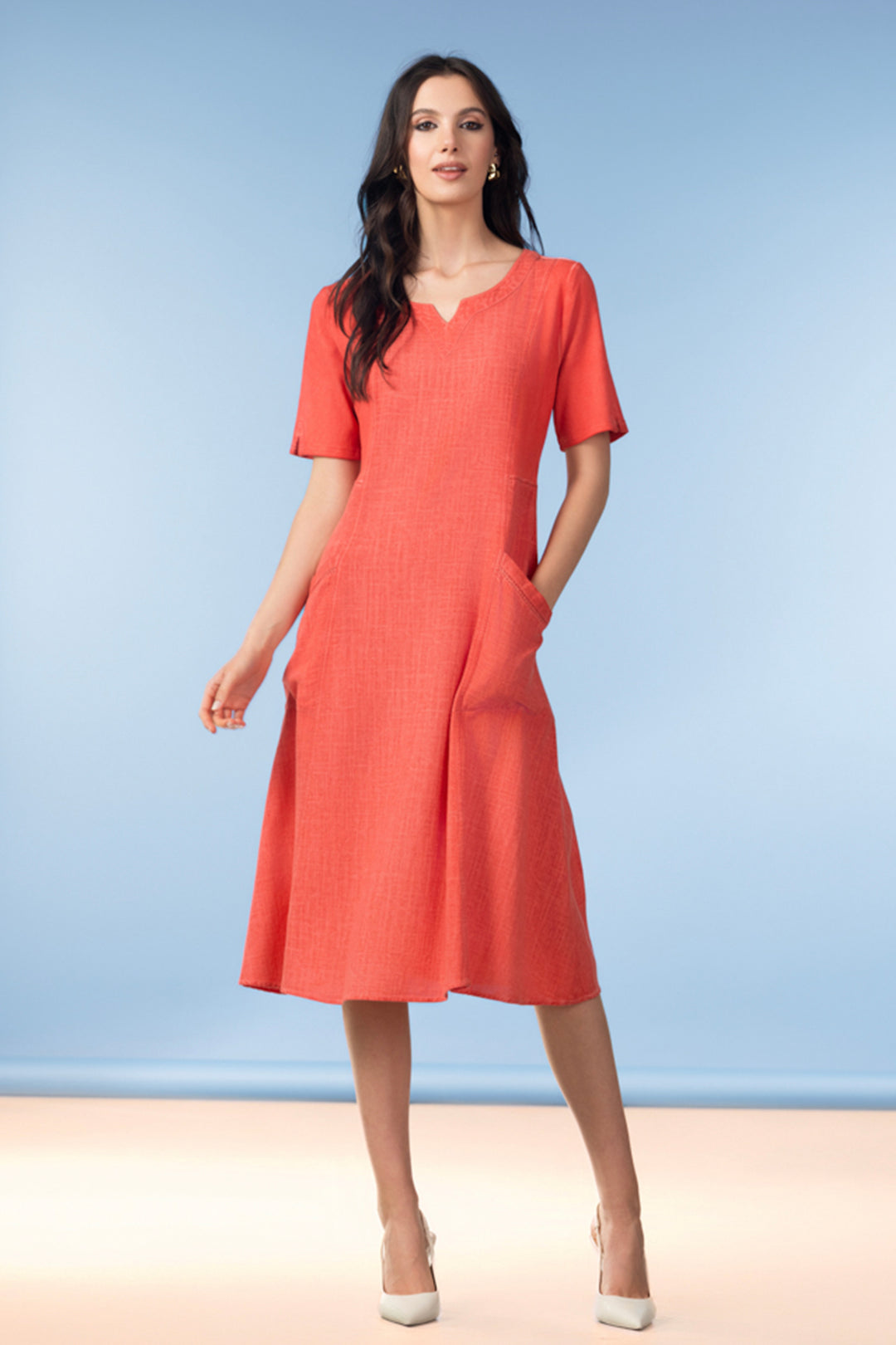 Woman wearing a coral short sleeve dress against a light blue background