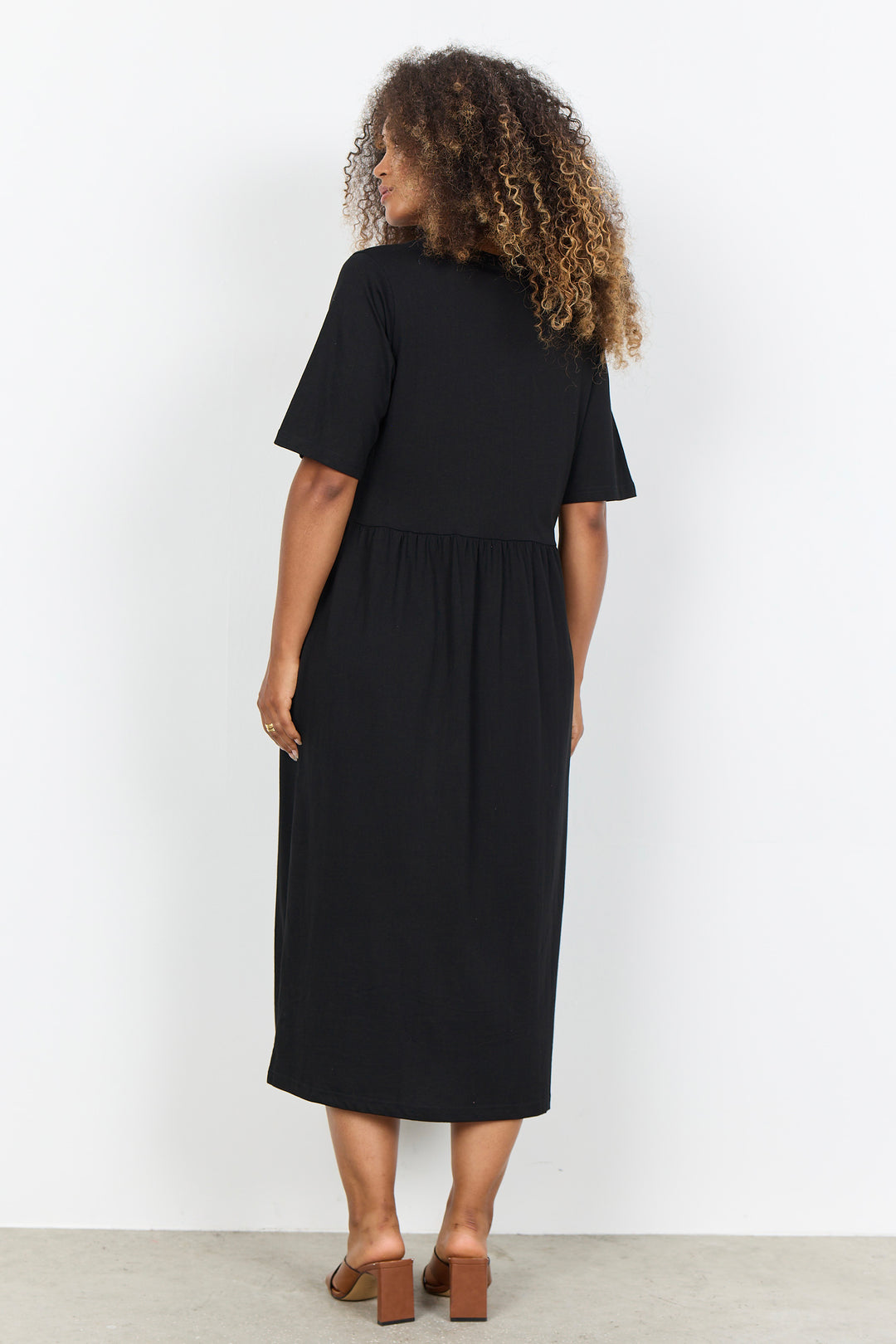 Woman wearing a midi length t-shirt dress on a white background. 