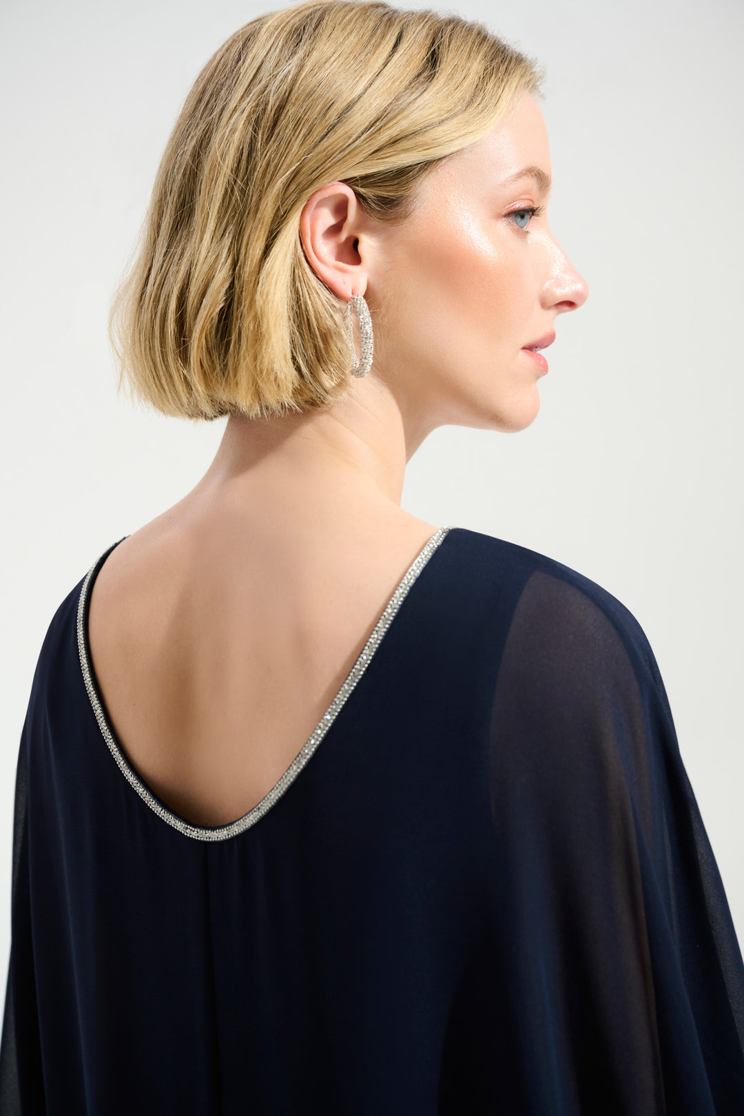 Woman wearing a dark blue dress with a silver trim on a plain background
