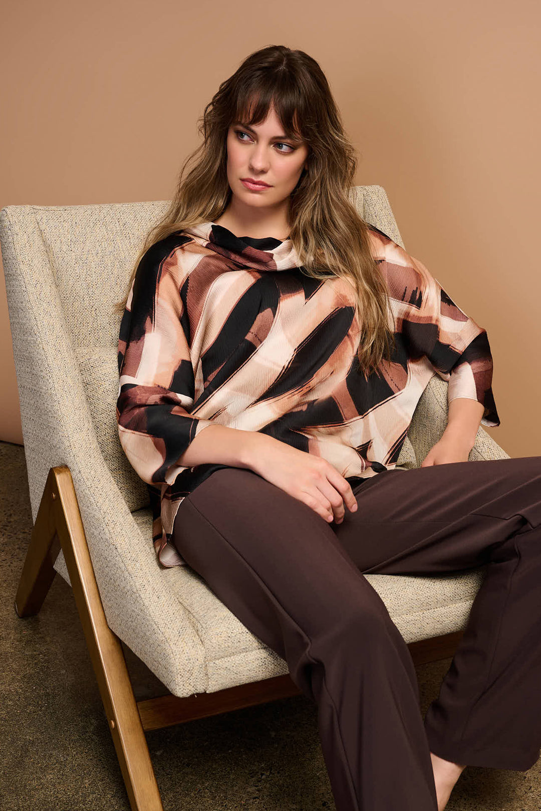 Woman sitting on a chair wearing a patterned cowl neck top. 