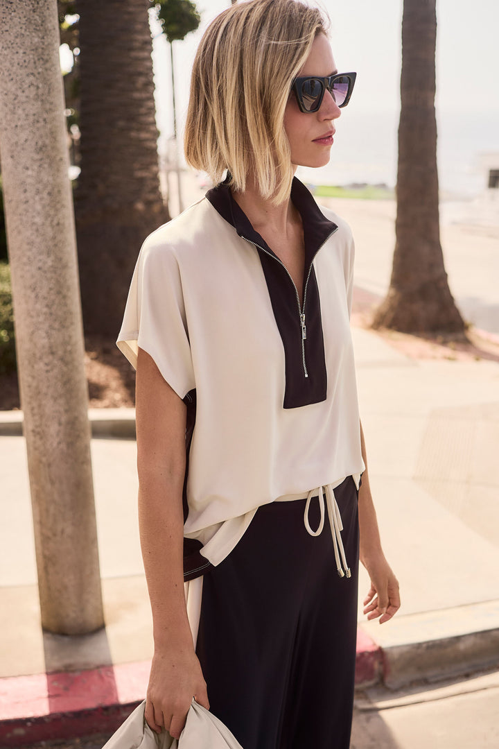 Woman wearing a white and black colourblock zipper top with sunglasses, standing outdoors.