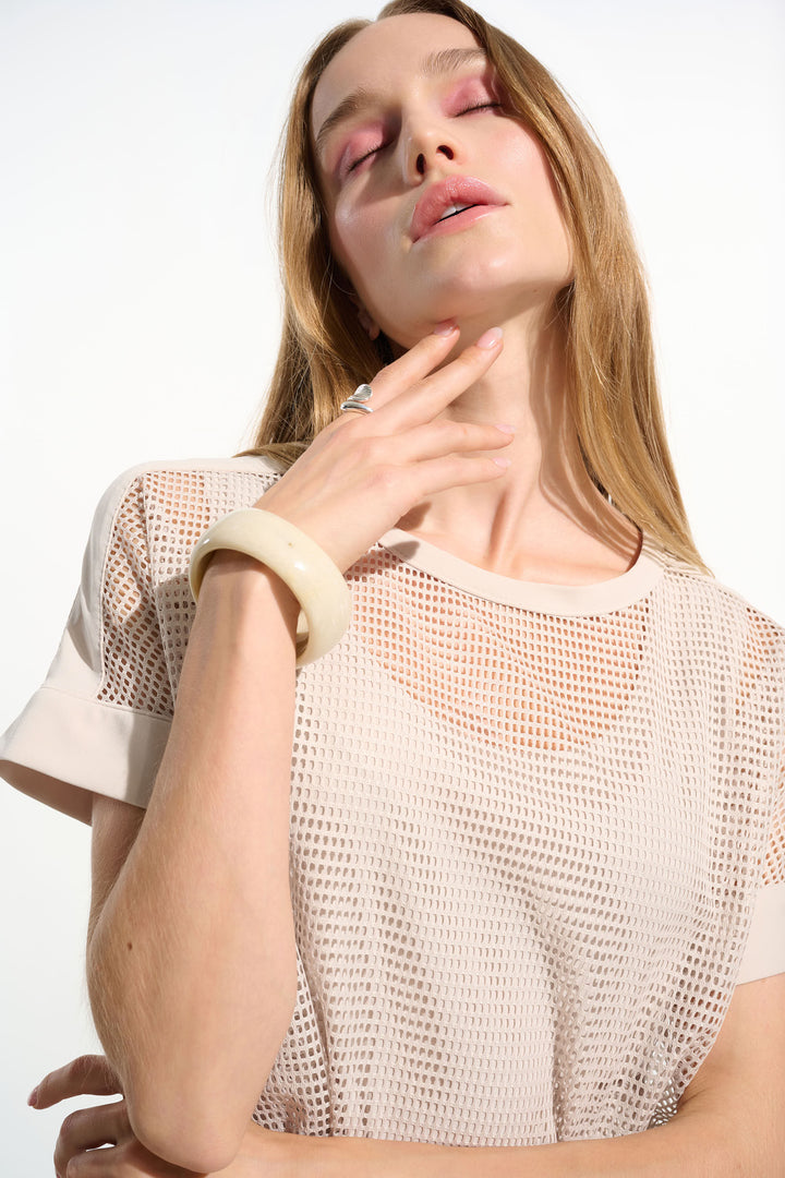 Woman wearing a beige mesh top with a plain background