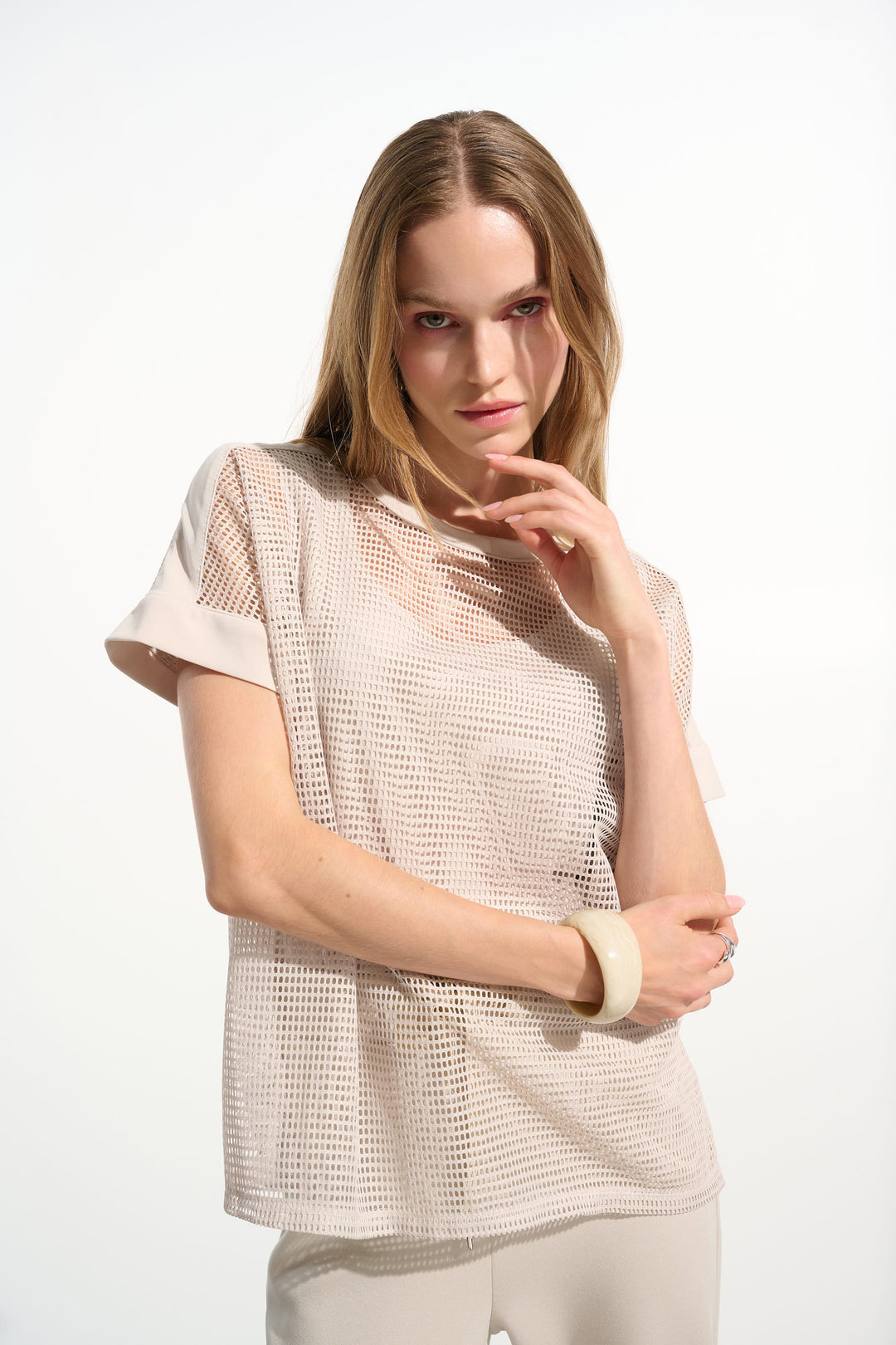Woman wearing a beige mesh top with short sleeves on a white background
