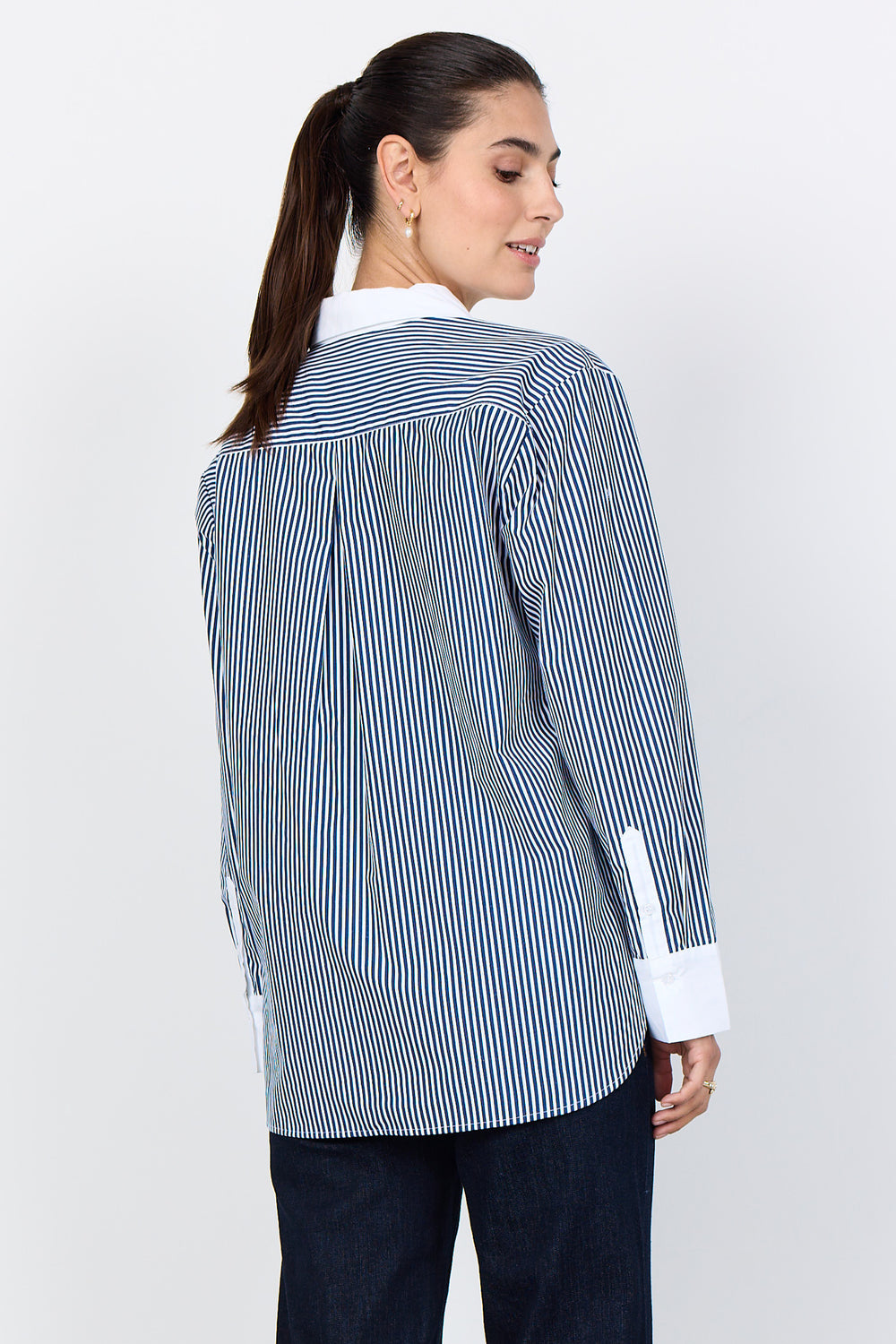 Woman wearing a blue and white striped shirt with a white collar on a plain background