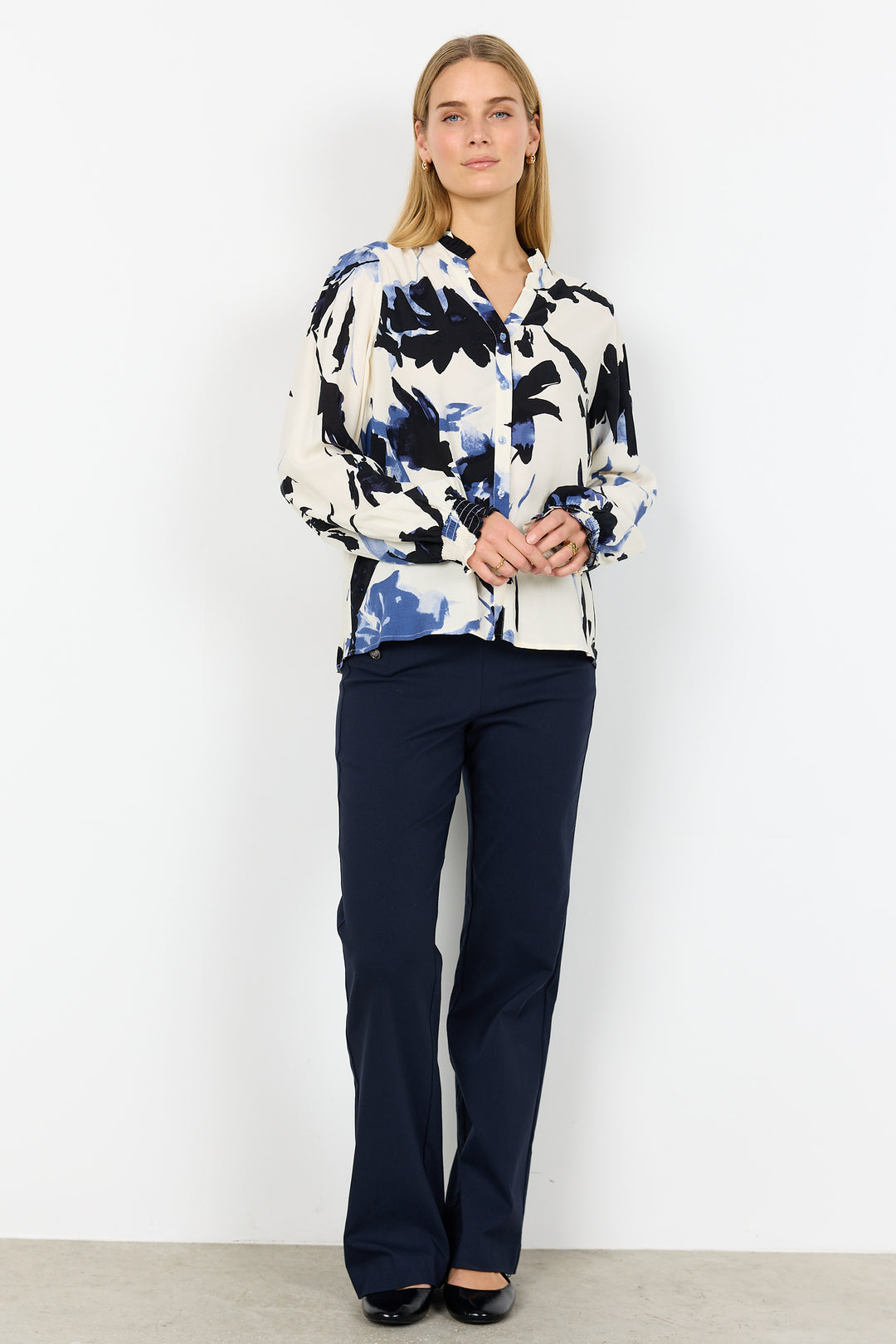 Woman wearing a patterned blouse and navy pants against a white background