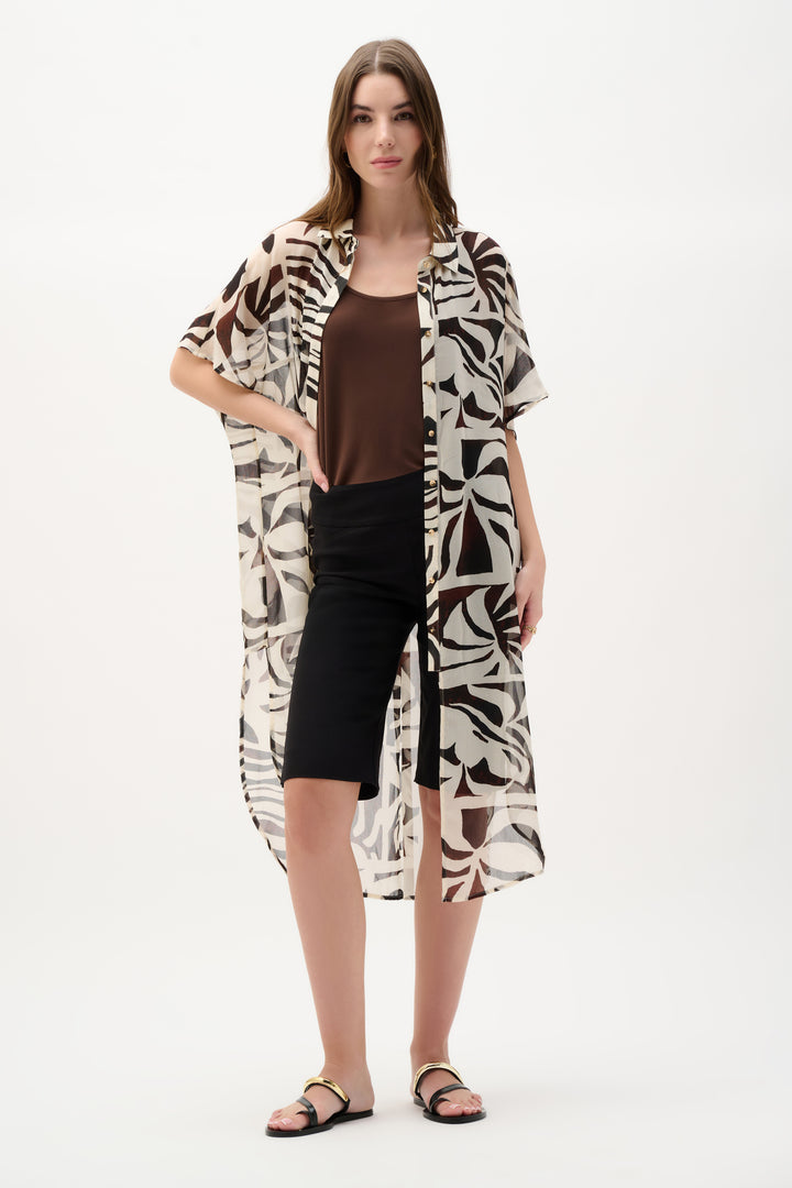 Woman wearing a patterned tunic blouse over a brown top and black shorts on a white background