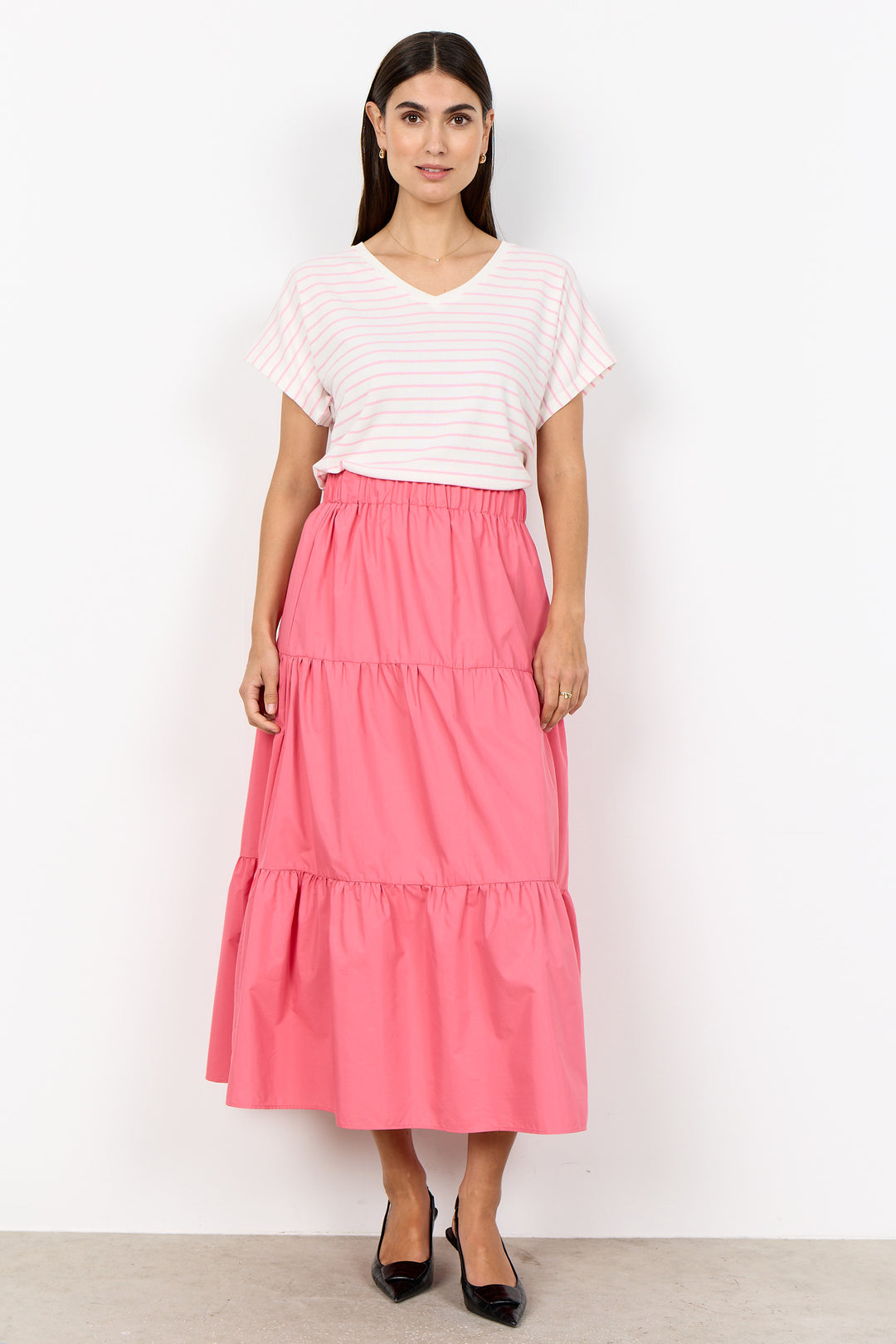Woman wearing a white top and pink tiered skirt on a white background