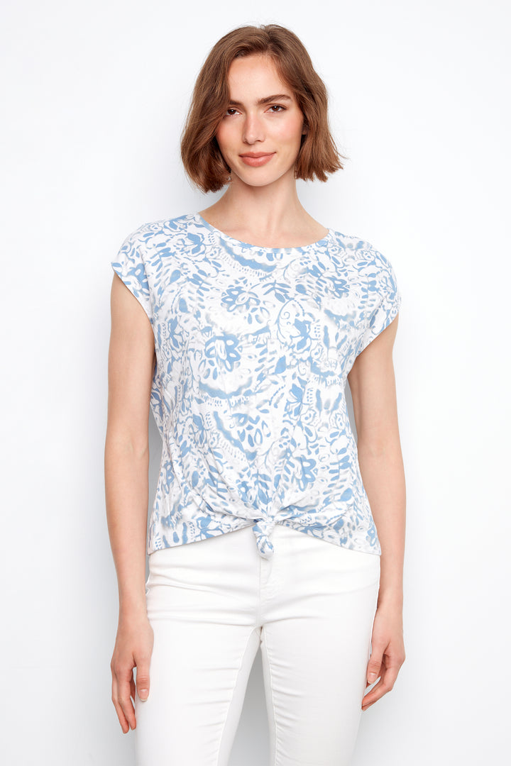 Woman wearing a blue floral top and white pants on a white background