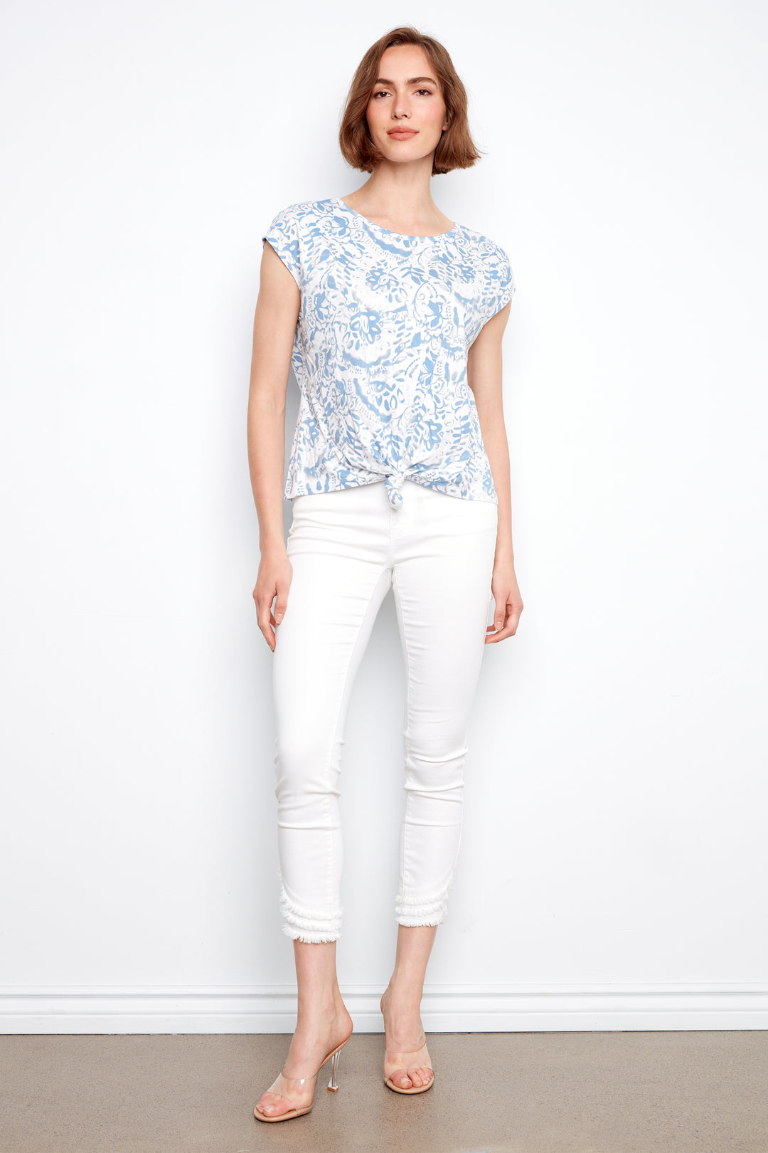 Woman wearing a floral top and white pants against a plain background
