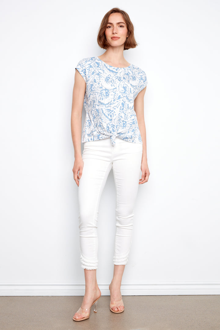 Woman wearing a floral top and white pants against a plain background