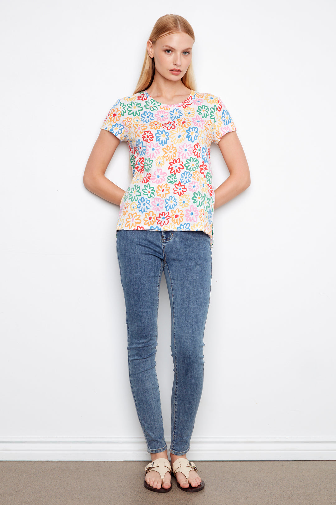 Woman wearing a colorful floral top and blue jeans against a white background