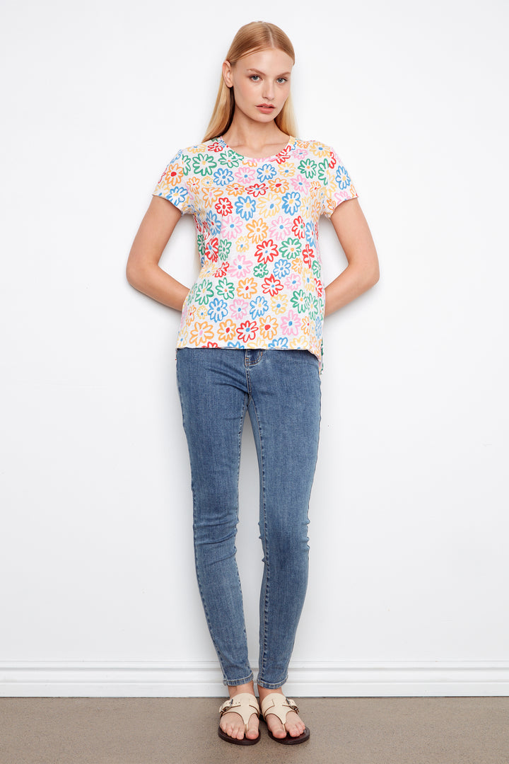 Woman wearing a colorful floral top and blue jeans against a white background