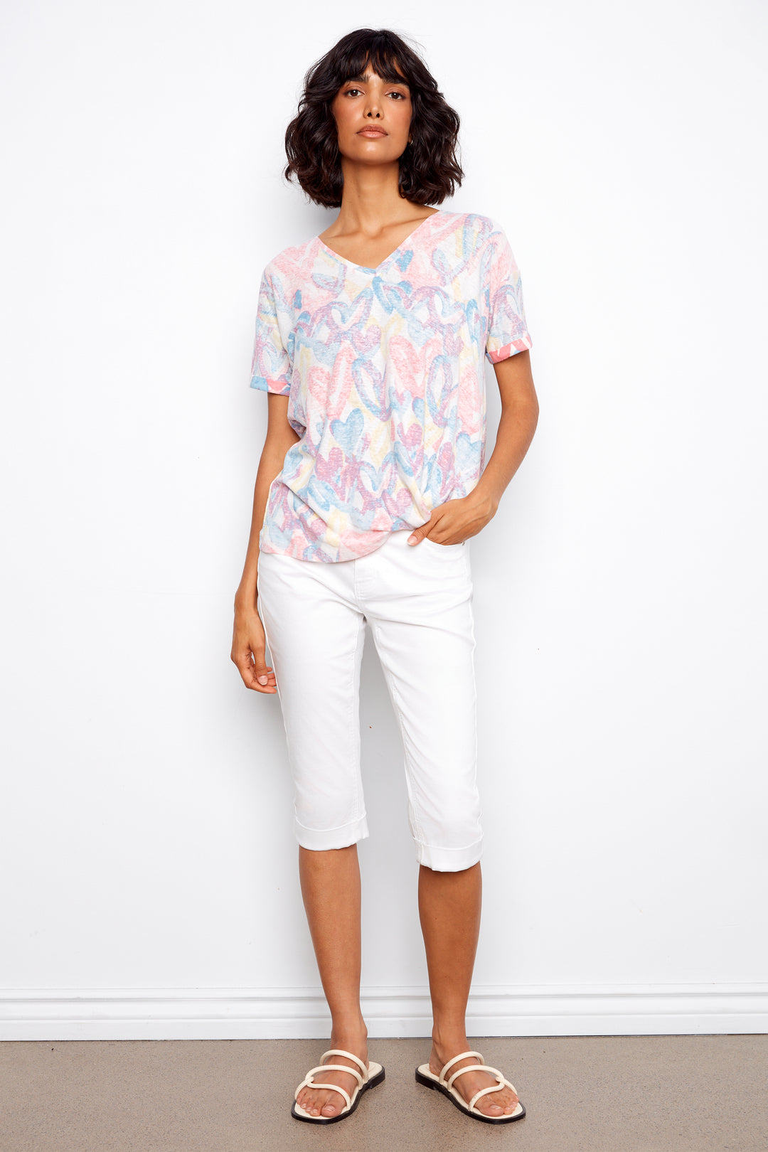 Woman wearing a patterned top and white pants against a plain background