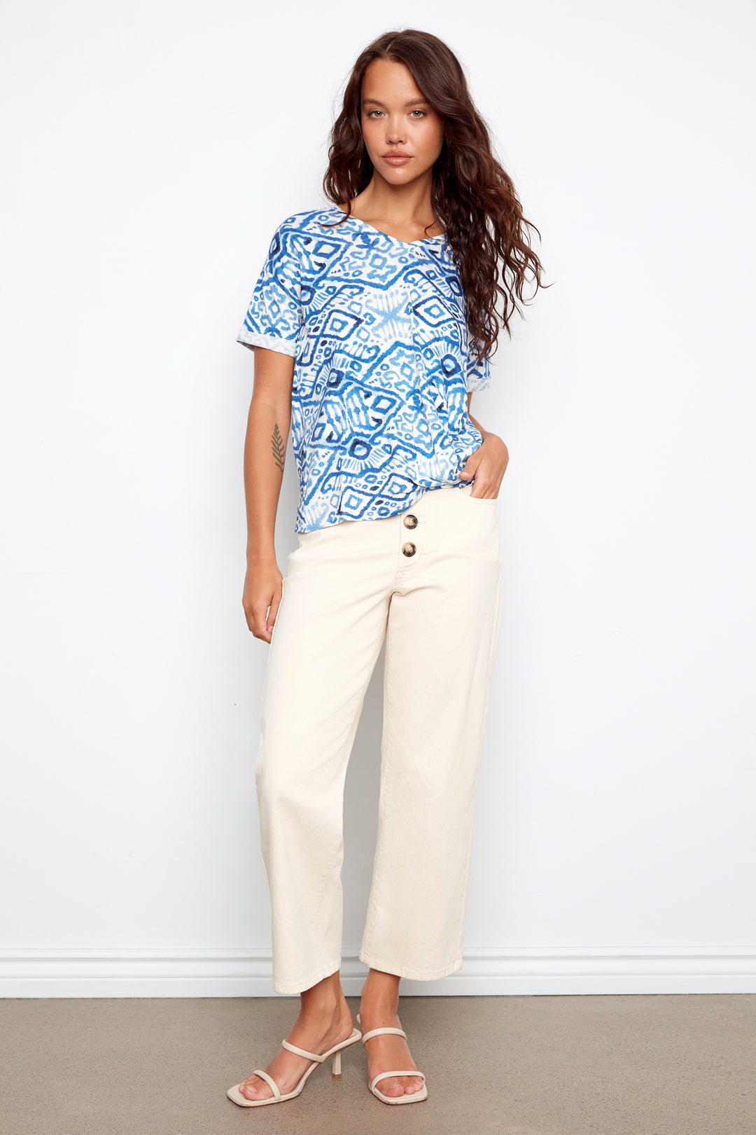 Woman wearing a blue patterned top and white pants against a white background