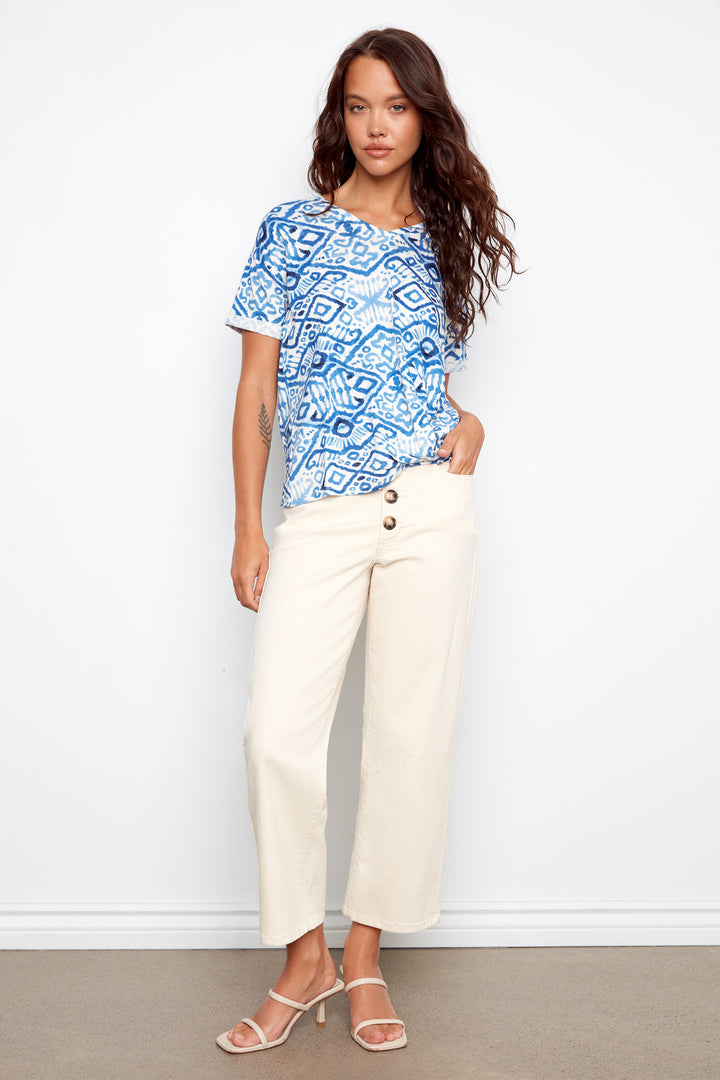 Woman wearing a blue patterned top and white pants against a white background