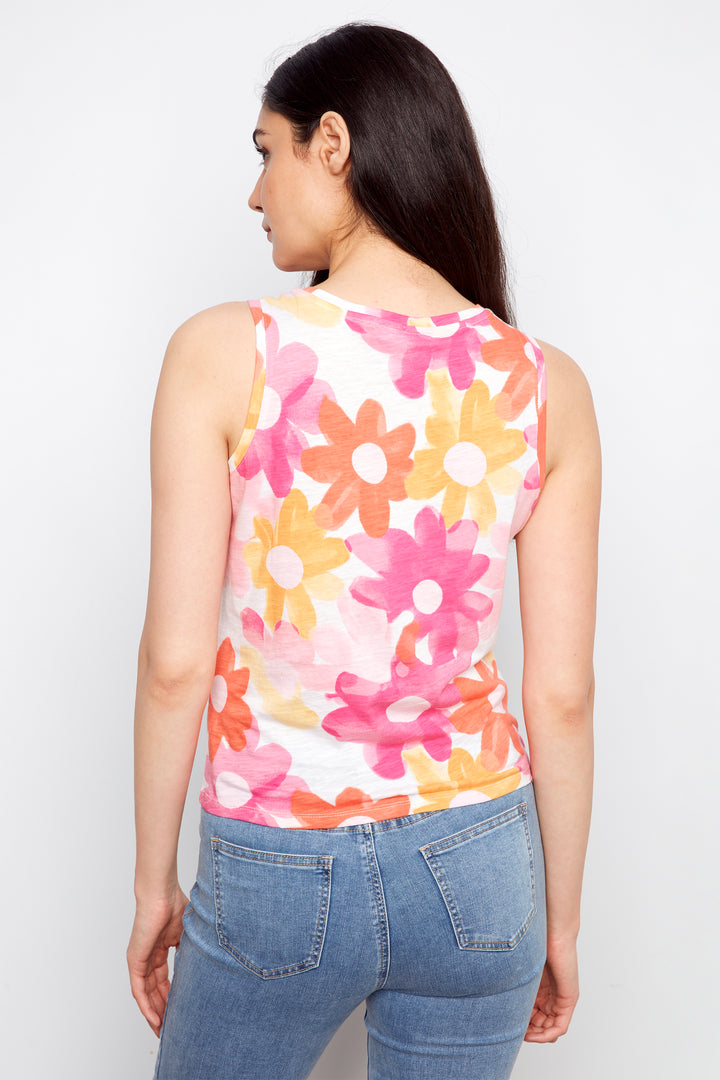 Woman wearing a sleeveless top with colorful floral pattern and blue jeans on a white background