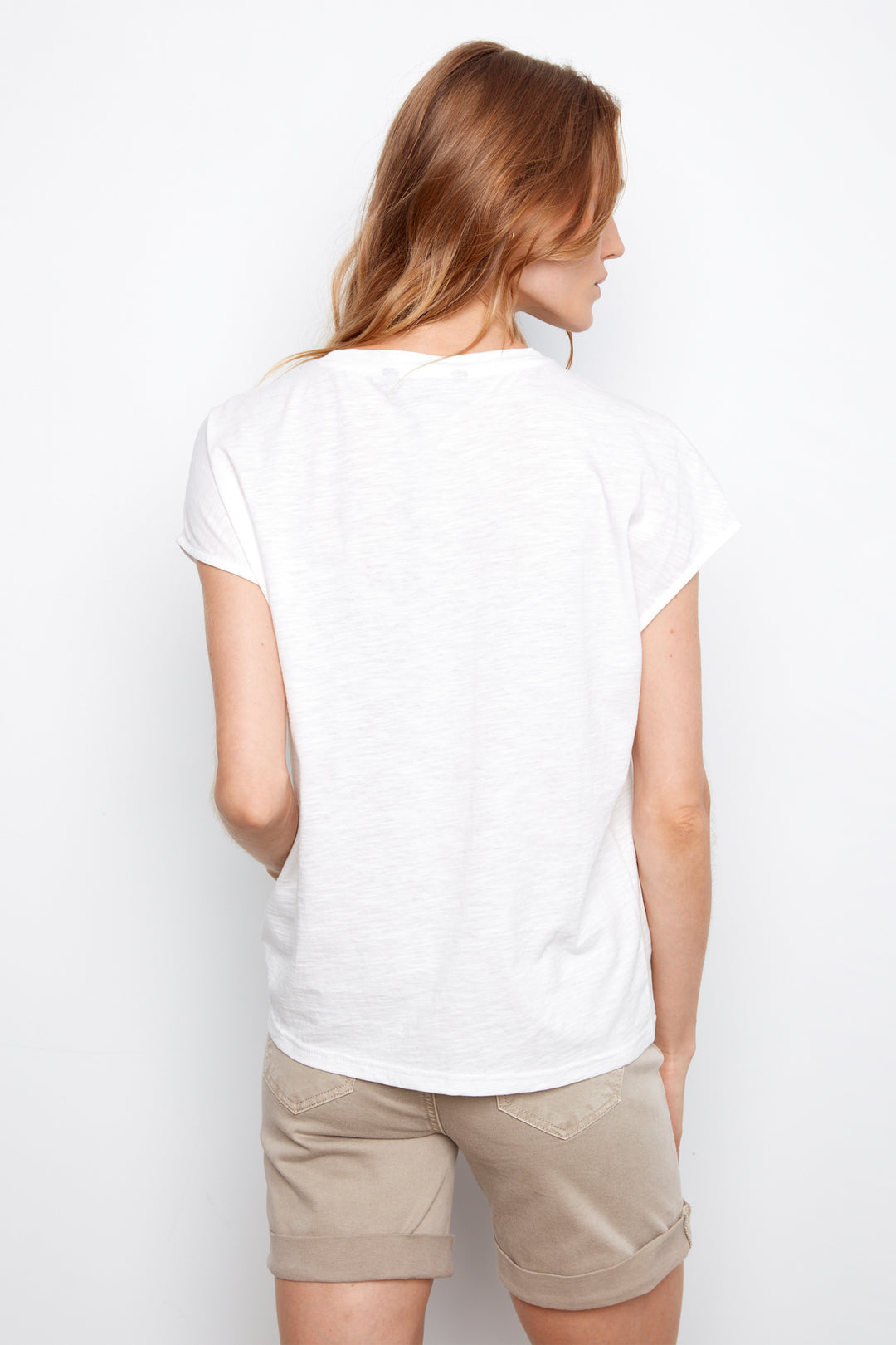 Woman wearing a white t-shirt and beige shorts on a plain background