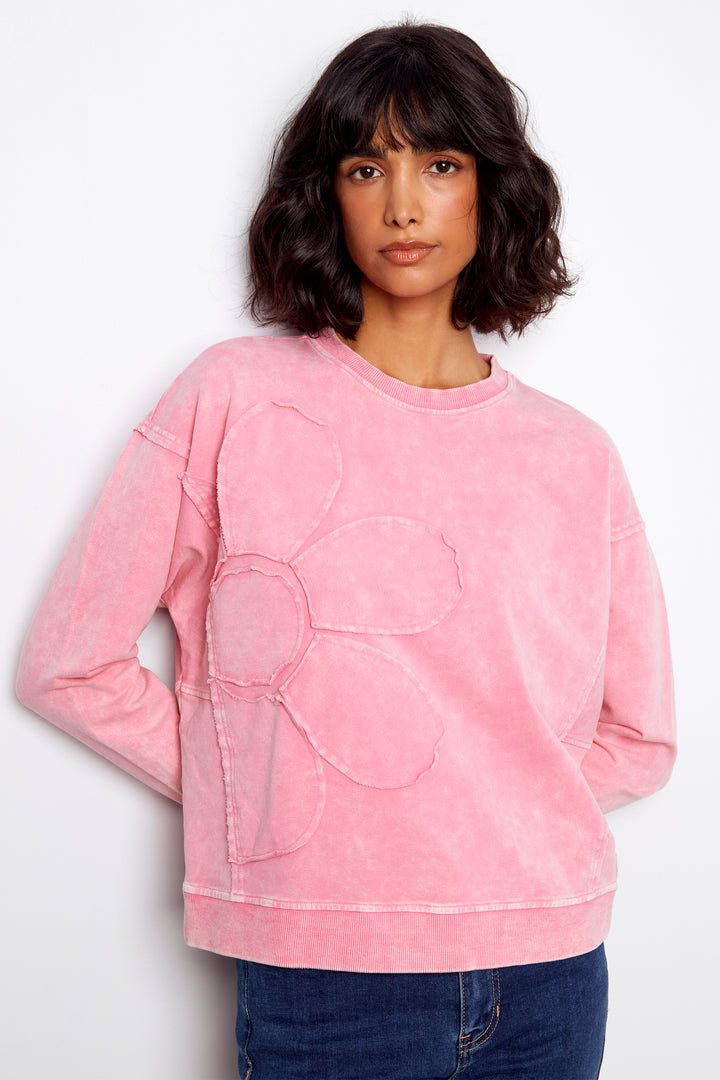 Person wearing a pink sweatshirt with a large logo on a white background