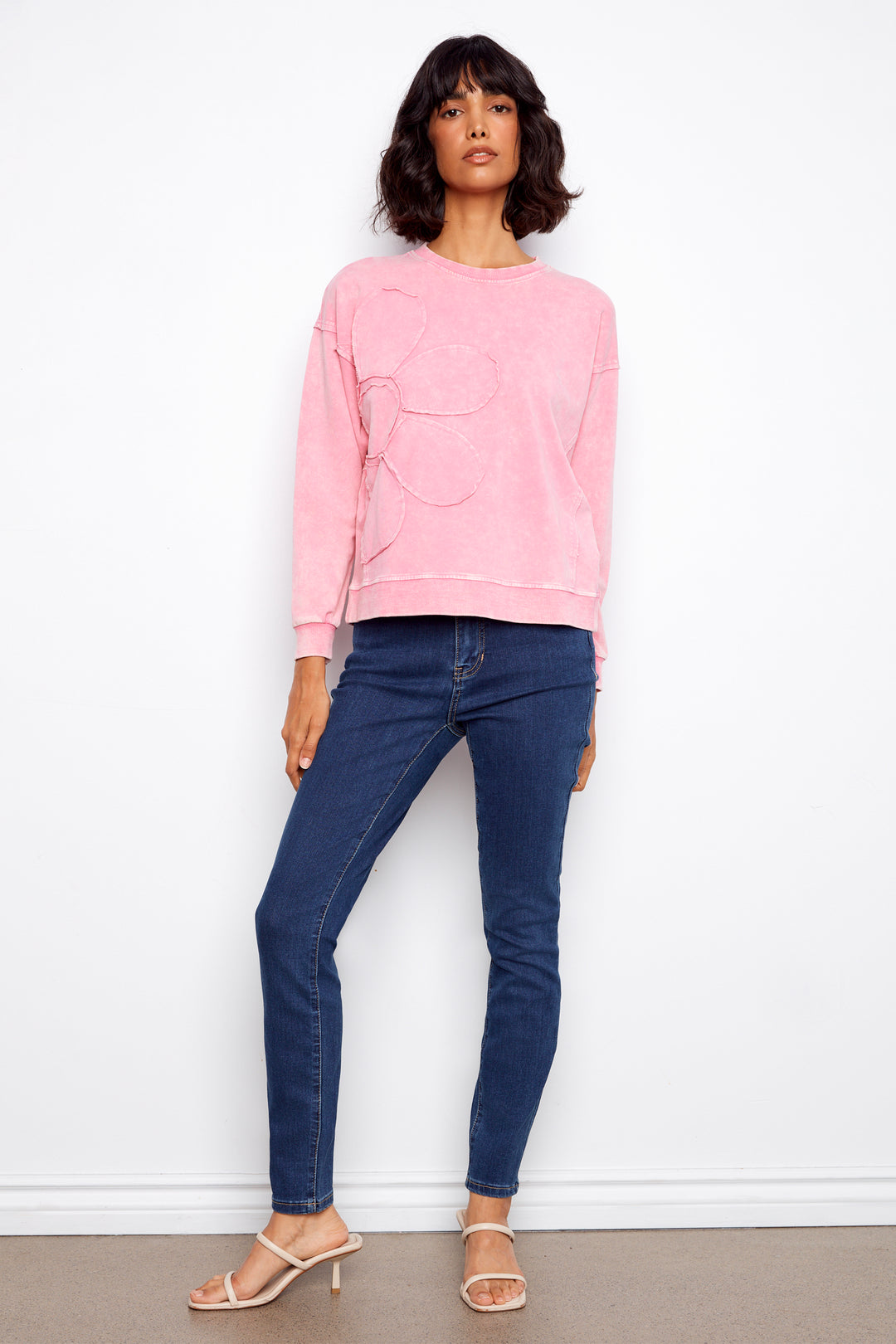 Woman wearing a pink sweatshirt and blue jeans against a white background