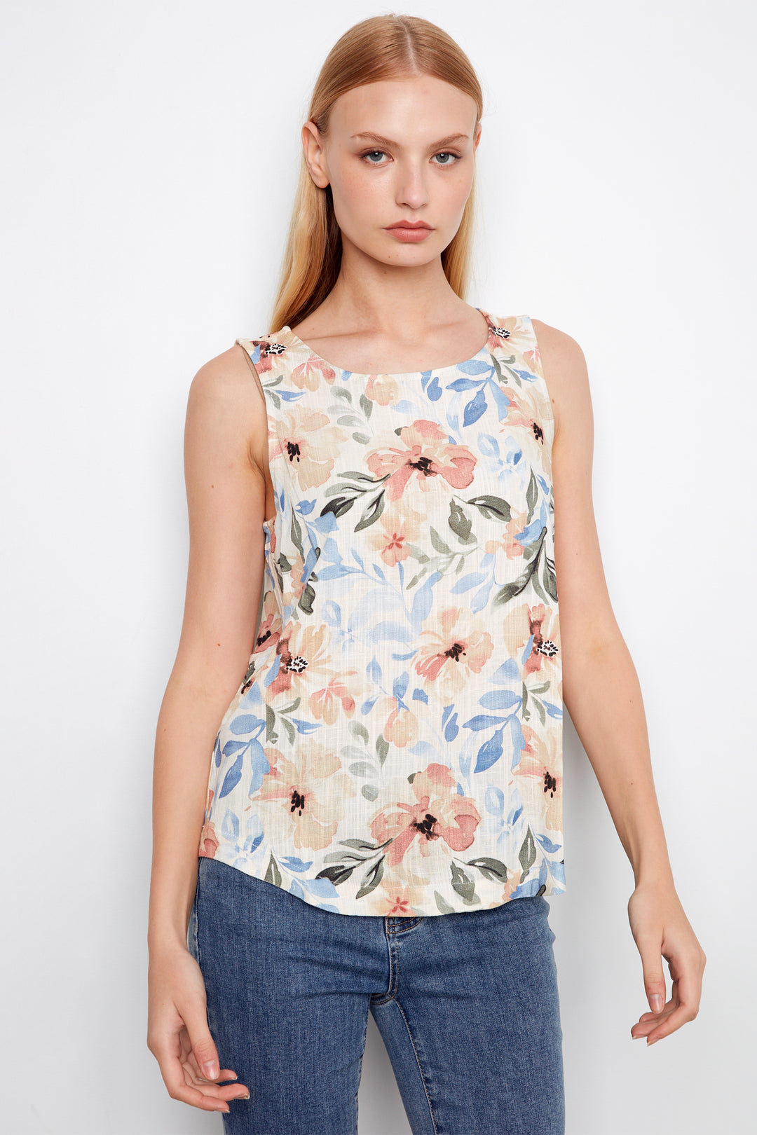 Woman wearing a floral sleeveless top and blue jeans on a white background