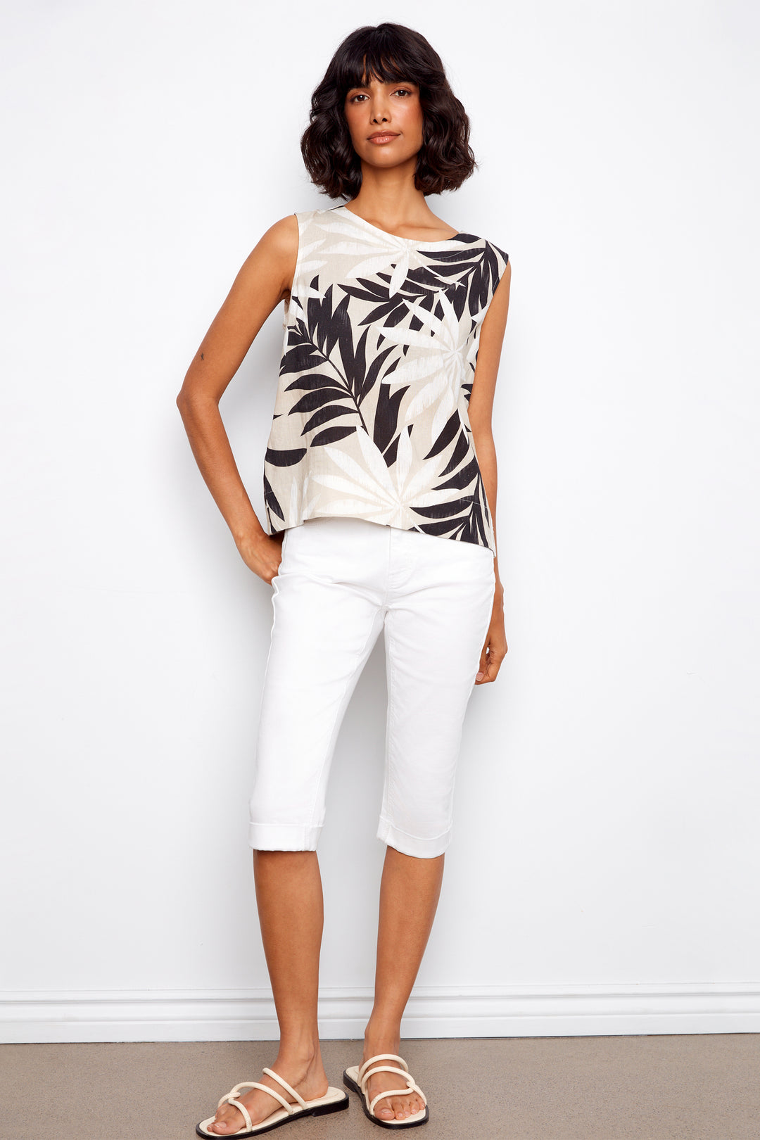 Woman wearing a sleeveless top with leaf pattern and white pants against a white background