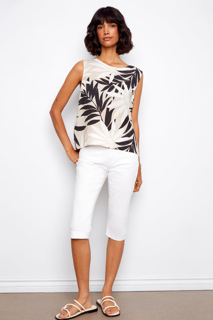 Woman wearing a sleeveless top with leaf pattern and white pants against a white background