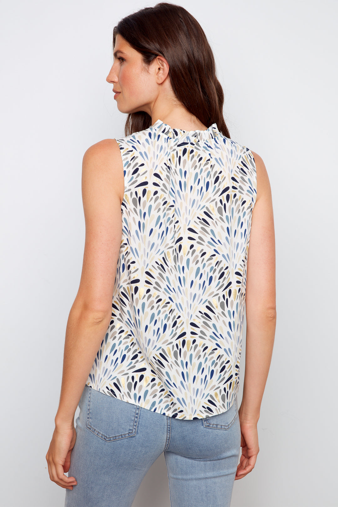 Woman wearing a sleeveless patterned top and jeans on a plain background