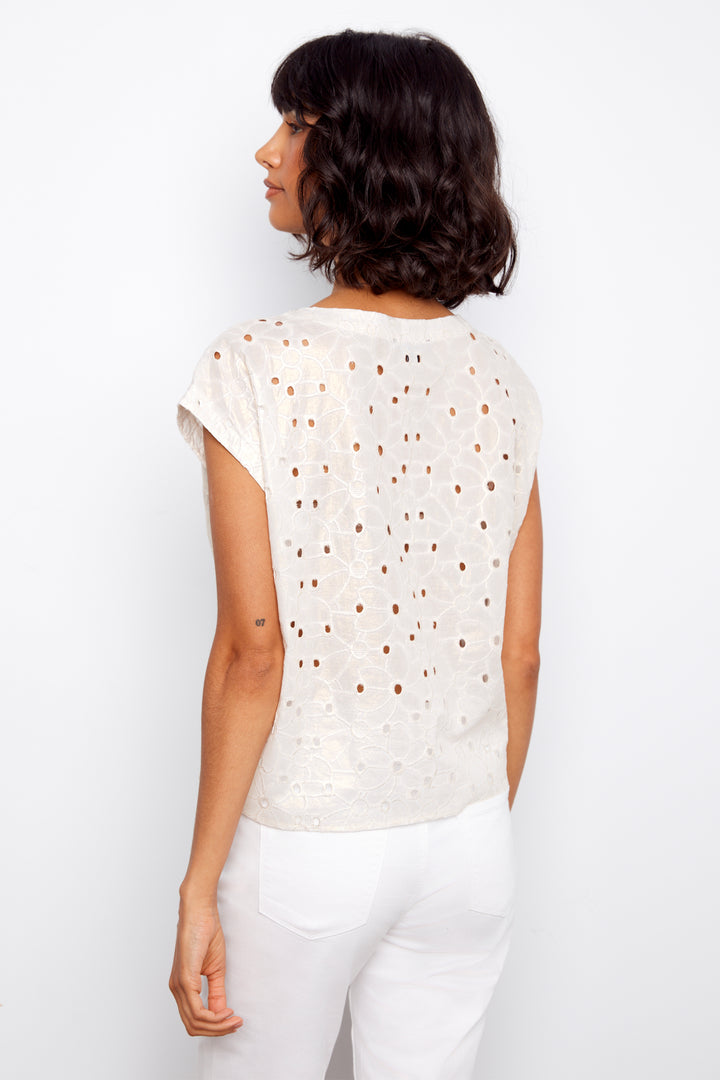 Woman wearing a white lace top and white pants against a plain background