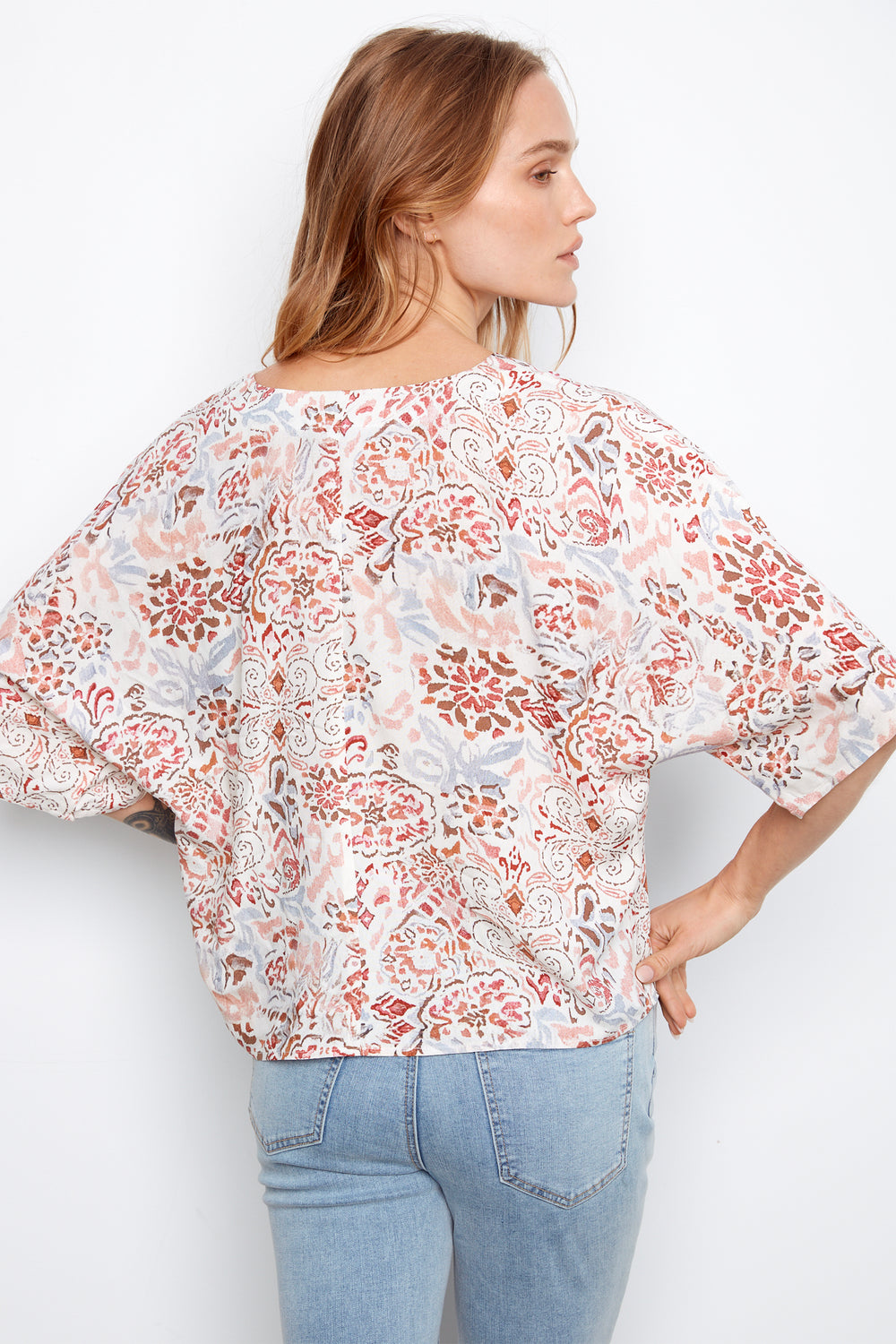 Woman wearing a floral blouse and light blue jeans on a white background
