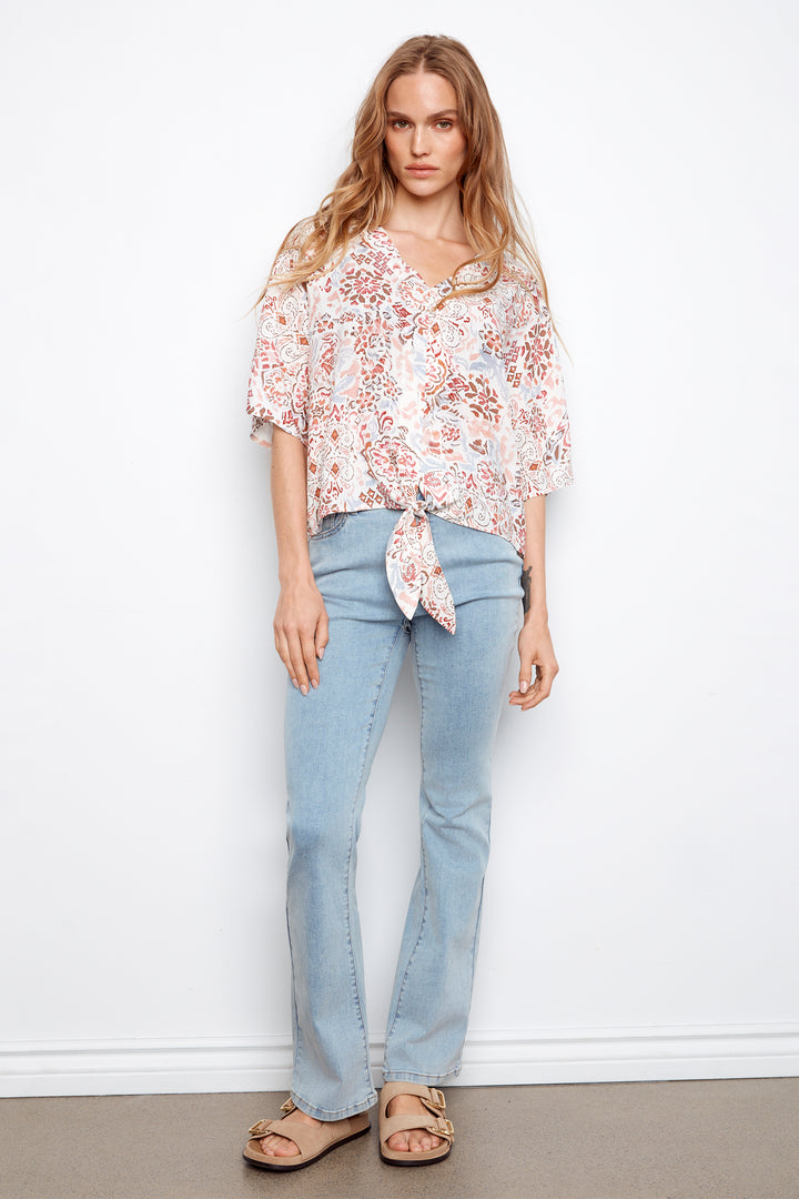Woman wearing a floral blouse and light blue jeans against a white background