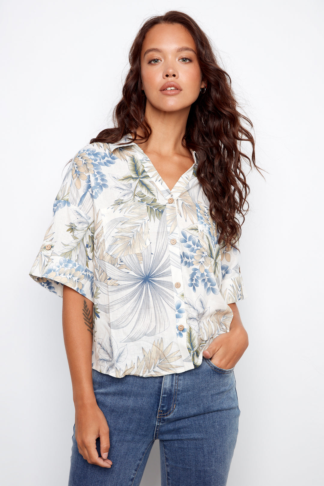 Woman wearing a floral blouse and jeans against a white background