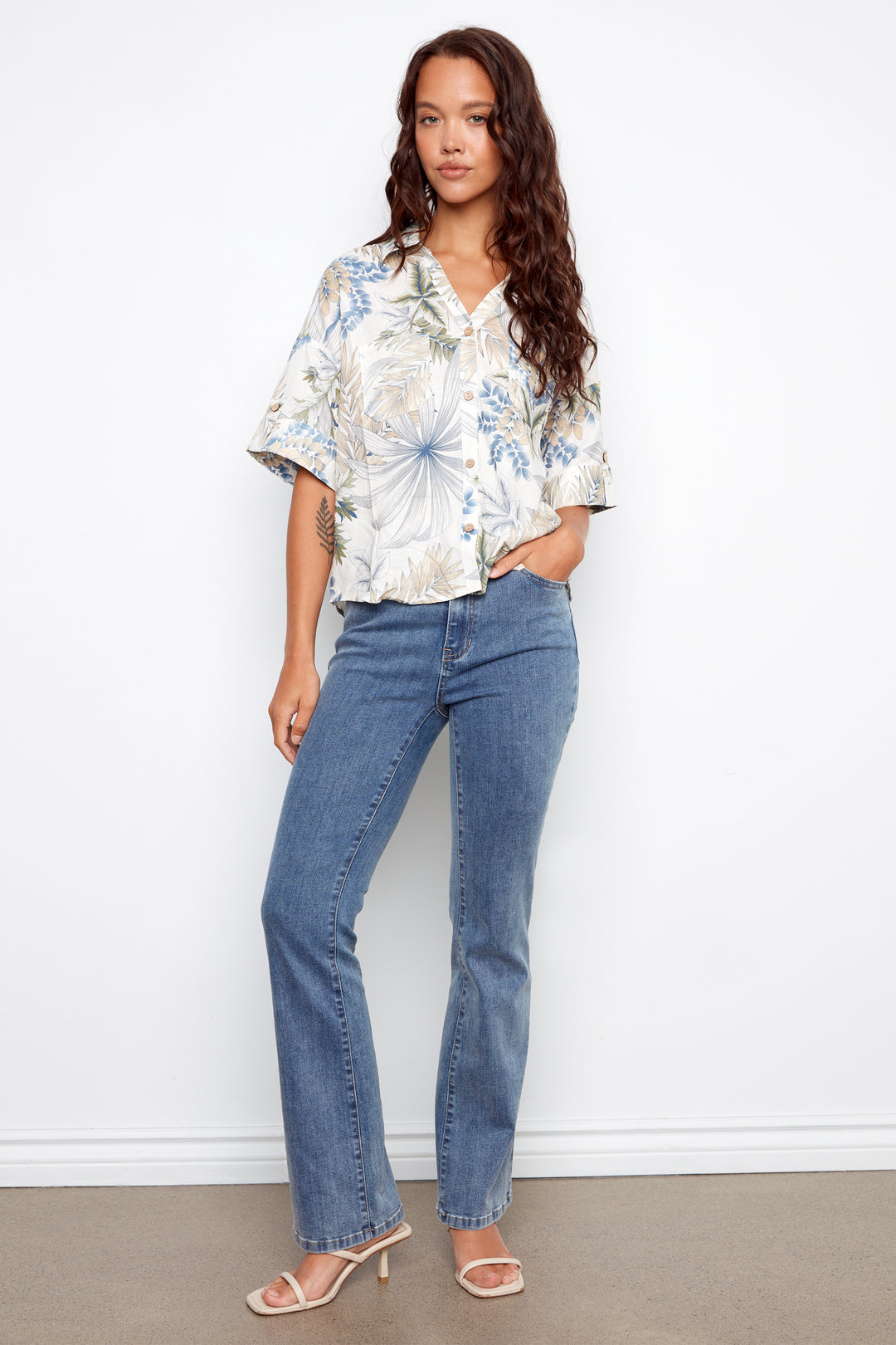 Woman wearing a floral blouse and blue jeans against a white background