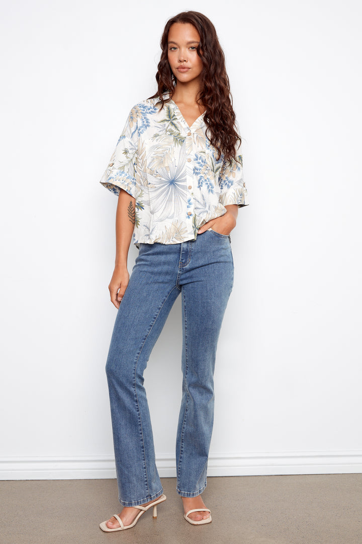 Woman wearing a floral blouse and blue jeans against a white background